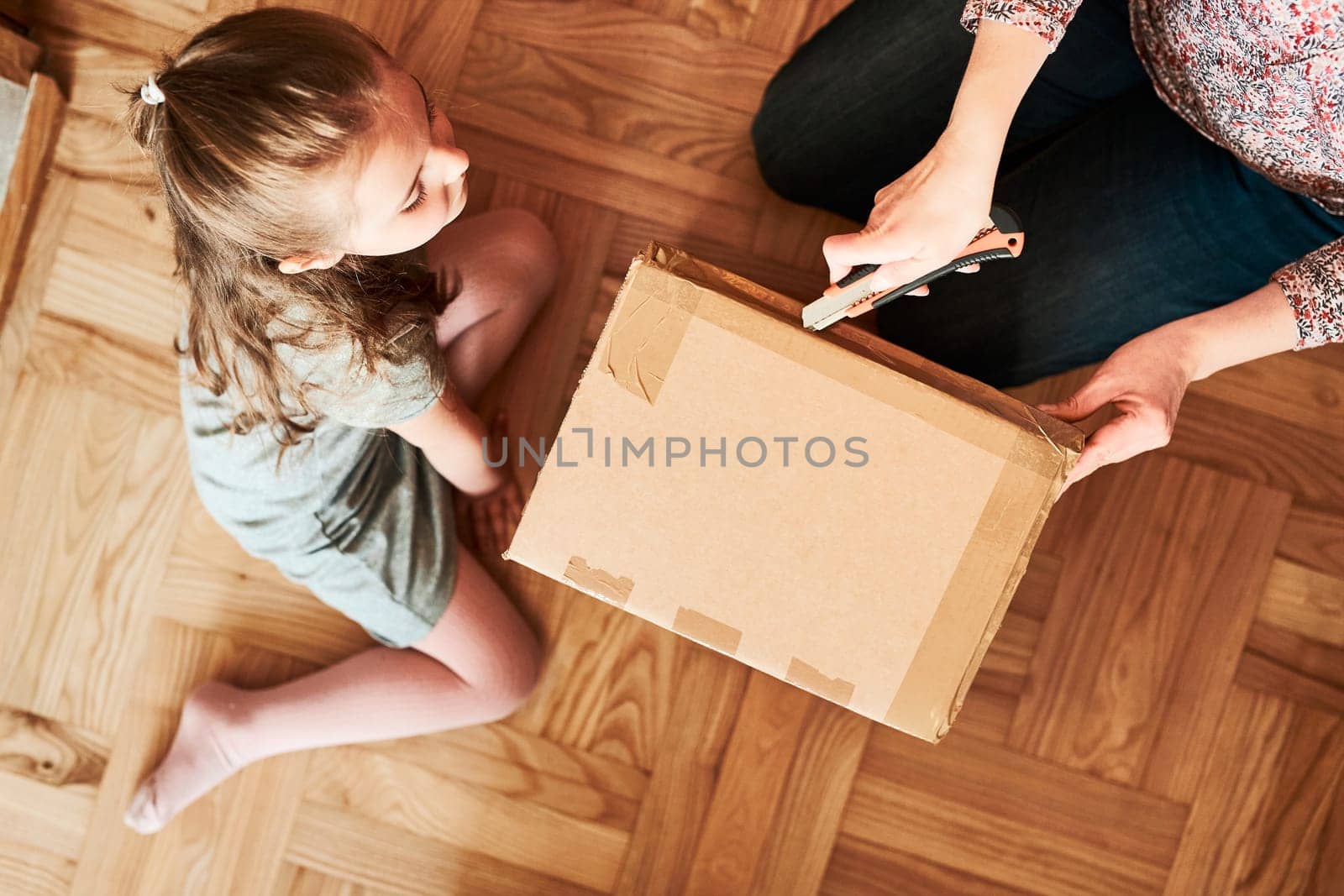 Woman unpacking a cardboard box parcel in room at home. Little girl waiting for opening a gift in package