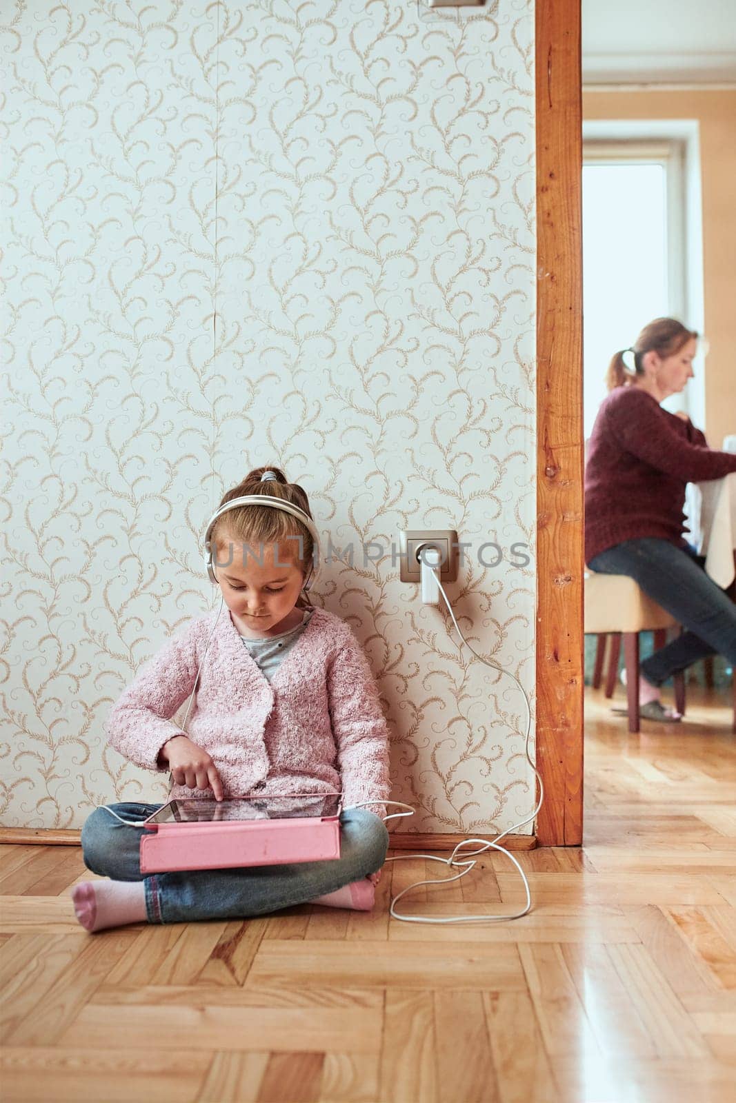 Little girl preschooler learning online solving puzzles playing educational games listetning to music and sounds using tablet and headpphones at home during pandemic quarantine