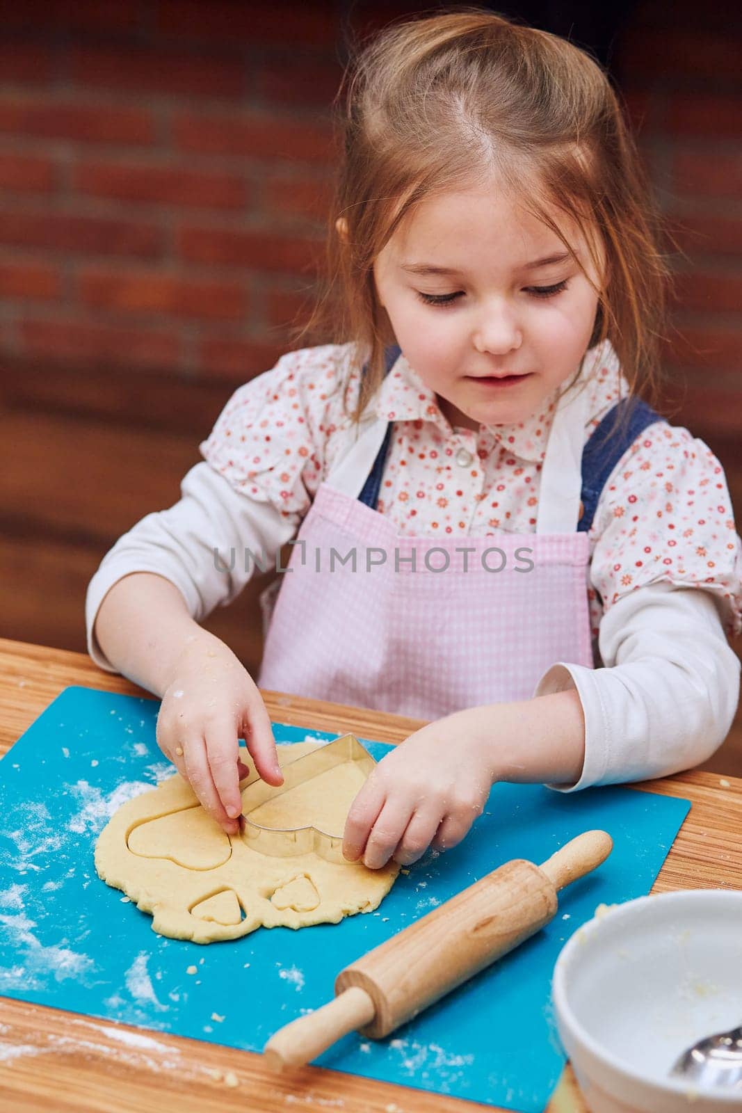 Little girl cutting the dough to heart shapes cookies. Kid taking part in baking workshop. Baking classes for children, aspiring little chefs. Learning to cook. Combining and stirring prepared ingredients. Real people, authentic situations