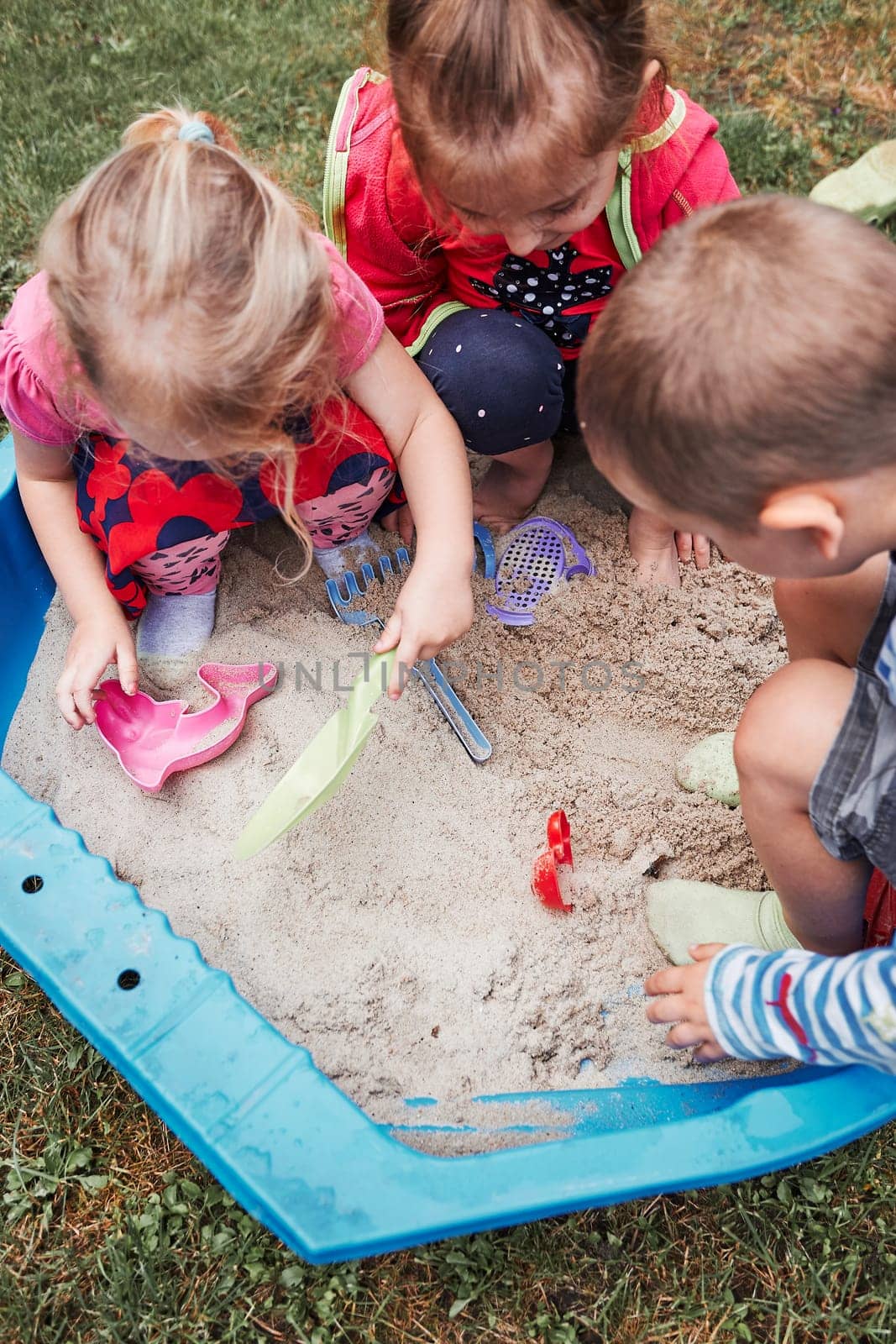 Children, little girls and boy, playing in sandbox in playground outside on summer day. Real people, authentic situations