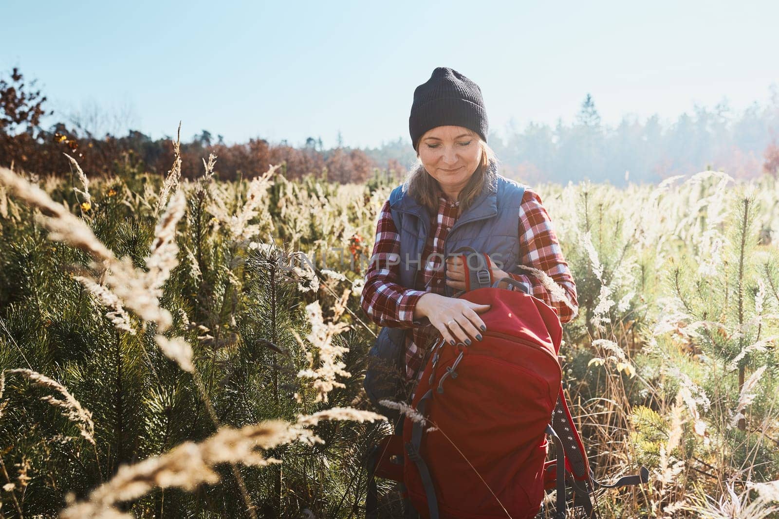 Young woman enjoying trip in mountains. Woman standing on trail. Woman with backpack hiking through tall grass along path in mountains. Spending summer vacation close to nature