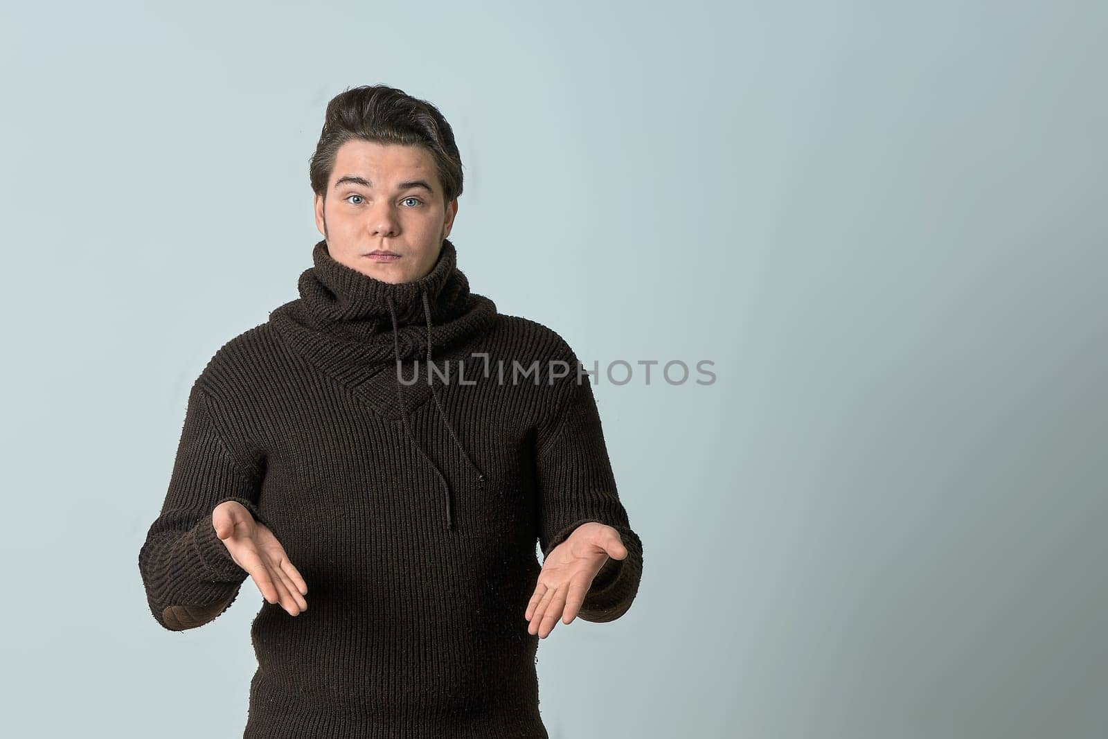 A man on a gray background in a brown sweater showing emotions, shows his hands. High quality photo