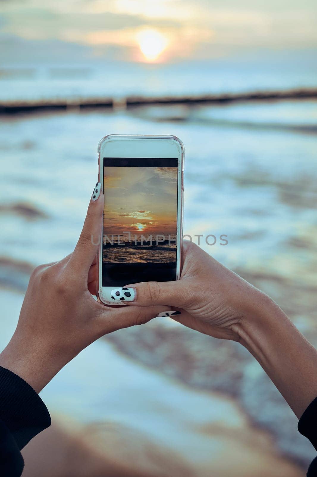 Young woman taking photos of sunset over sea using smartphone during summer trip. Rear view of girl holding smartphone and taking picture