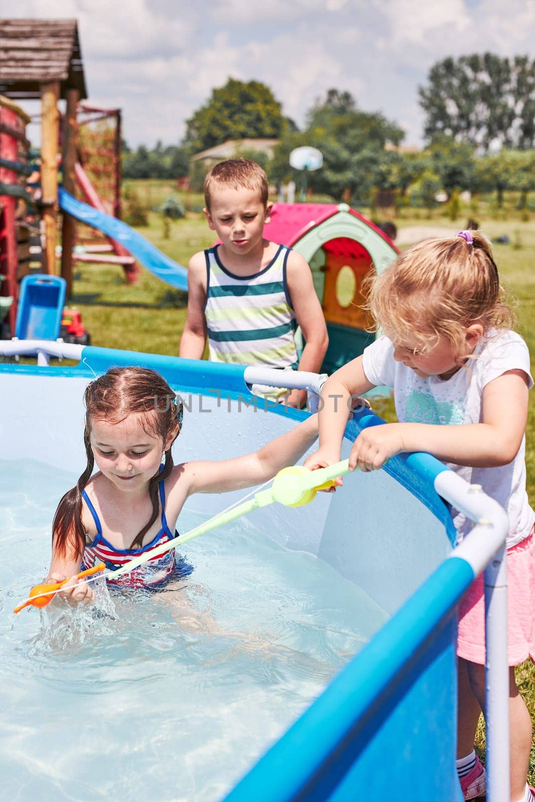 Children playing in a pool with fishing rod toy in a home garden. Kids having fun playing together on a summer sunny day