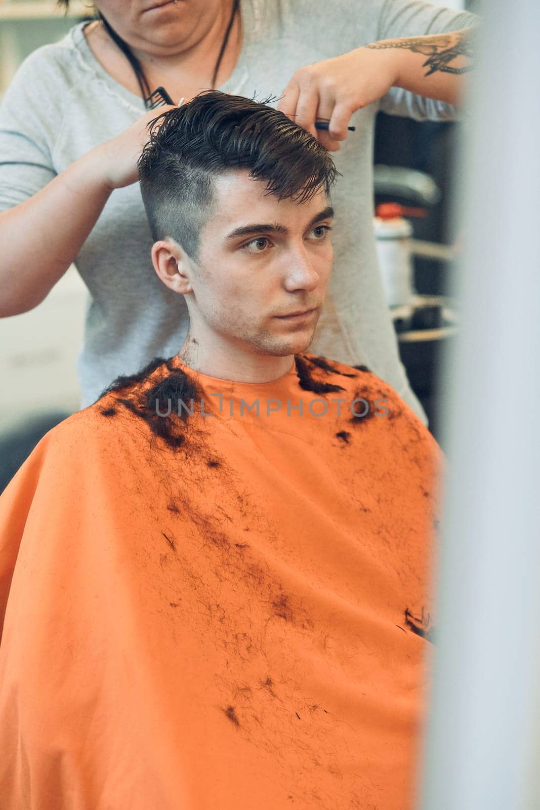 Hairdresser haircutting styling young man's hair in barbershop. Young woman working as a hairdresser in hair salon. Real people, authentic situations
