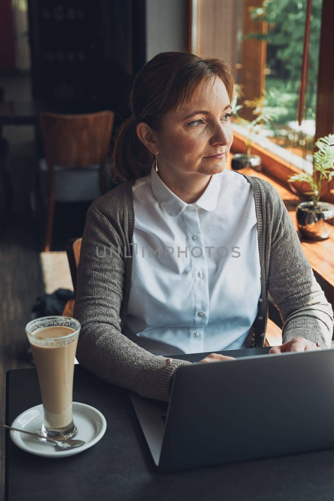 Relaxed businesswoman working remotely on her laptop computer contemplate managing her work sitting at the table in a cafe
