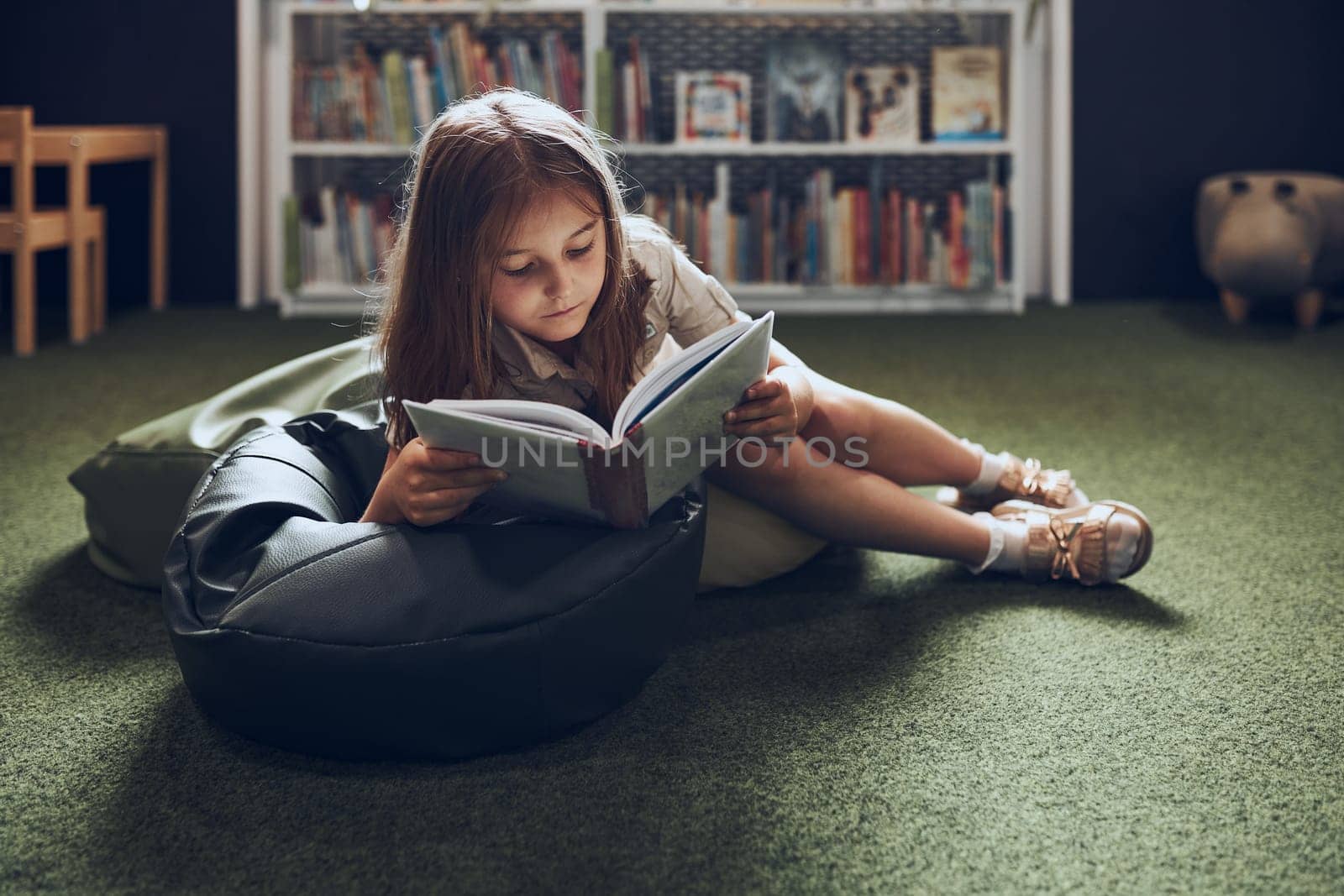 Schoolgirl reading book in school library. Primary school pupil is involved in book. Child doing homework. Smart girl learning from book. Benefits of everyday reading. Child curiosity
