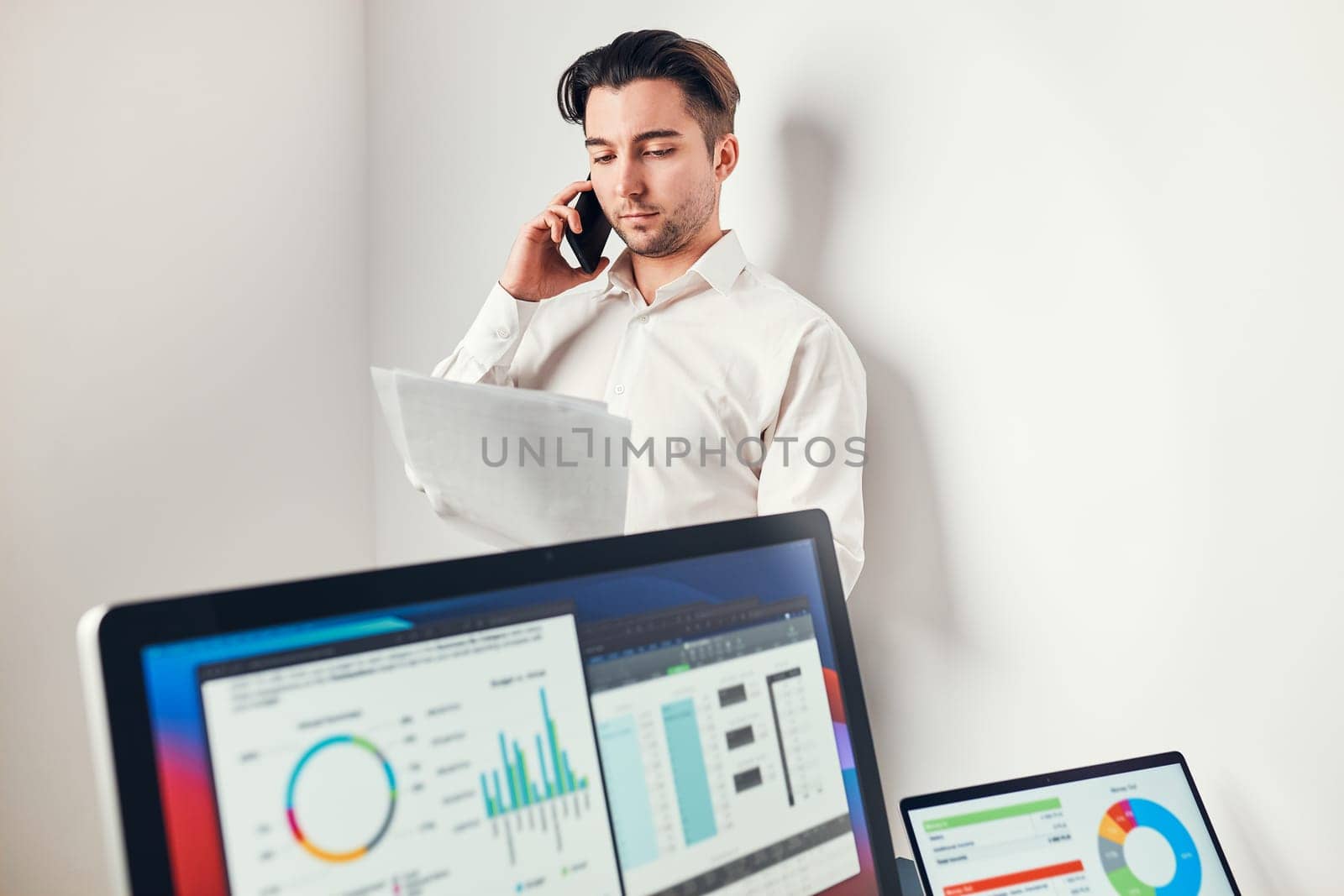Man entrepreneur having business  conversation on mobile phone. Businessman holding documents and smartphone working with data on charts and graphs in office. Man standing at desk