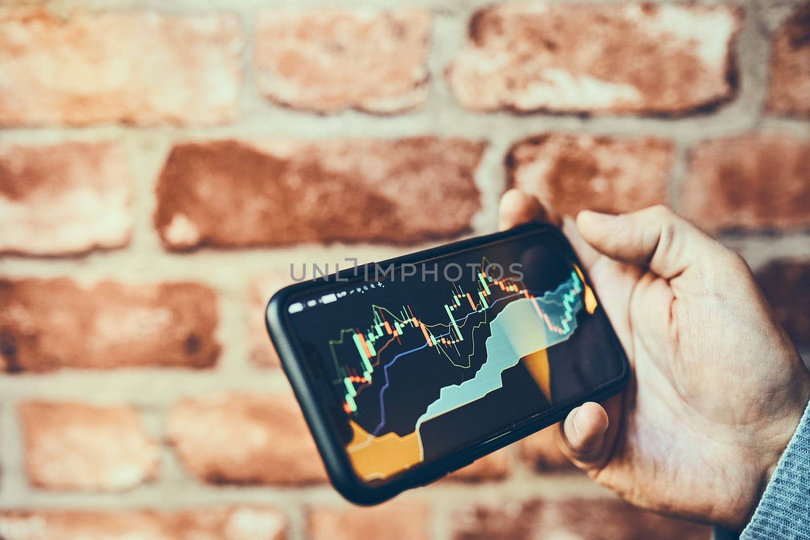 Person investing trading on stock cryptocurrency market using investing application on smartphone. Stock market investment in hand. Trader holding mobile phone looking at candle chart