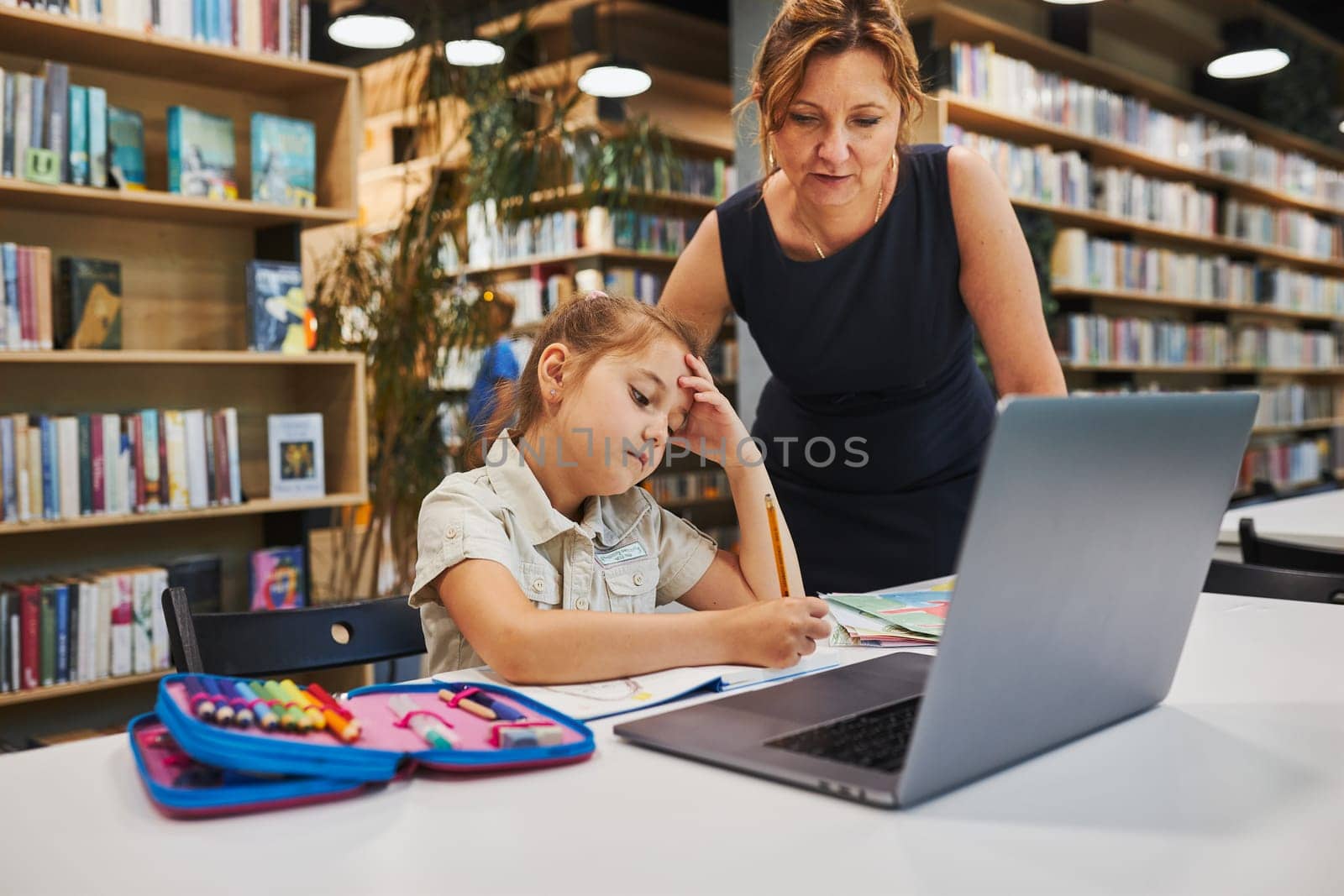 Teacher helping to solve and finish task. Bored little student girl doing her homework using laptop in after school club at primary school. Back to school. Child using technology on elementary computer science class. Smart little girl learning from educational application at school