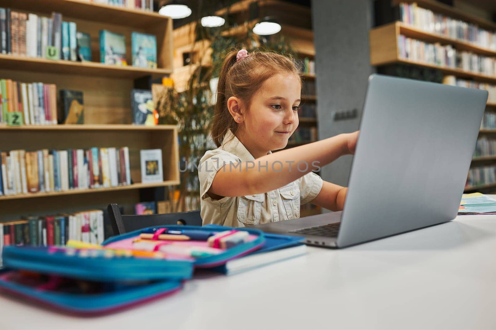 Positively engaged student doing her homework using laptop in after school club at primary school. Back to school. Child using technology on elementary computer science class. Smart little girl learning from educational application at school. Child solving riddles and puzzles on personal computer