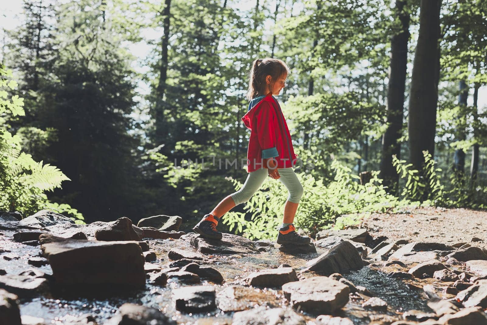 Child crossing mountain stream. Little girl walking in mountains, spending summer vacation close to nature