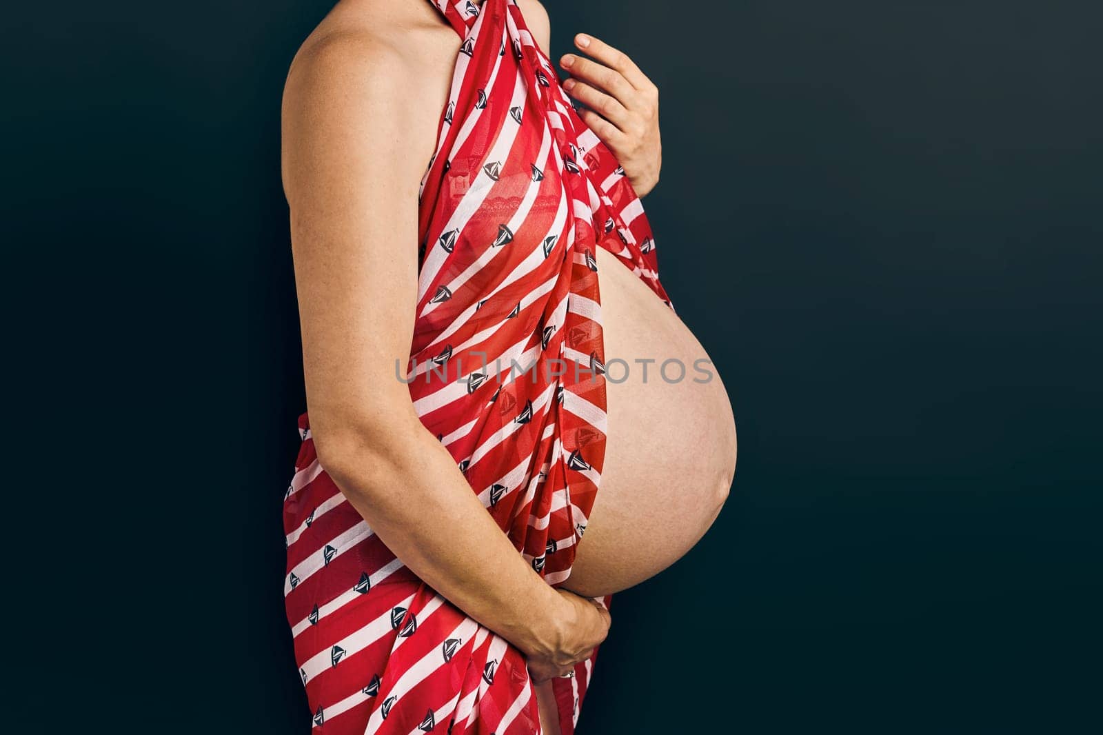 Pregnant woman touching her tummy standing over plain background. Pregnancy, expectation, motherhood concept