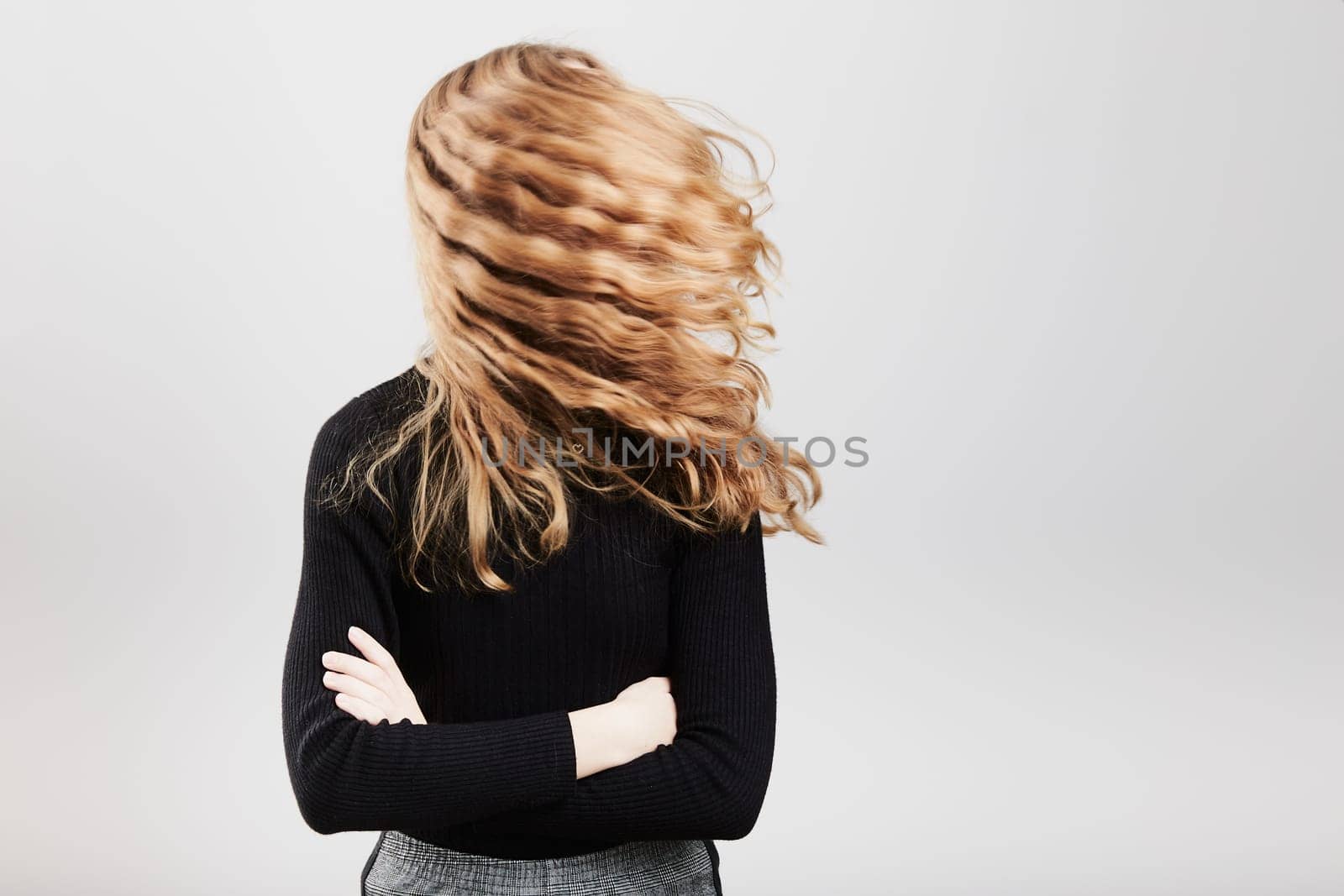 Portrait of pretty cheerful young woman waving tossing her hair holding arms crossed standing over a grey plain background