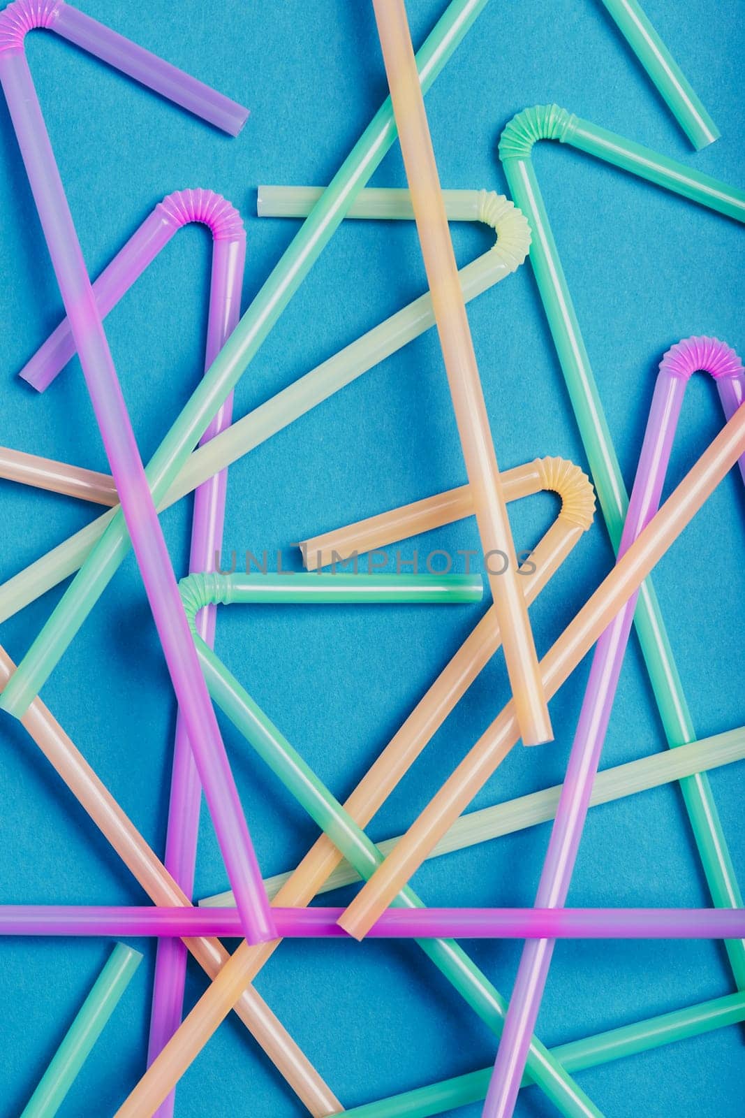 Heap of plastic drink straws scattered over blue background. Collecting plastic waste to recycling. Concept of plastic pollution and too many plastic waste. Copy space at the top