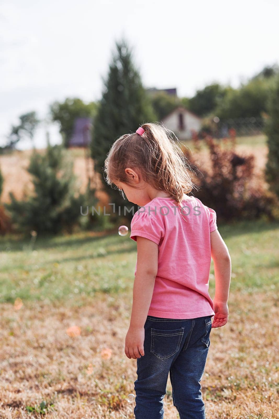 Little girl playing with soap bubbles outdoors on summer day. Real people, authentic situations