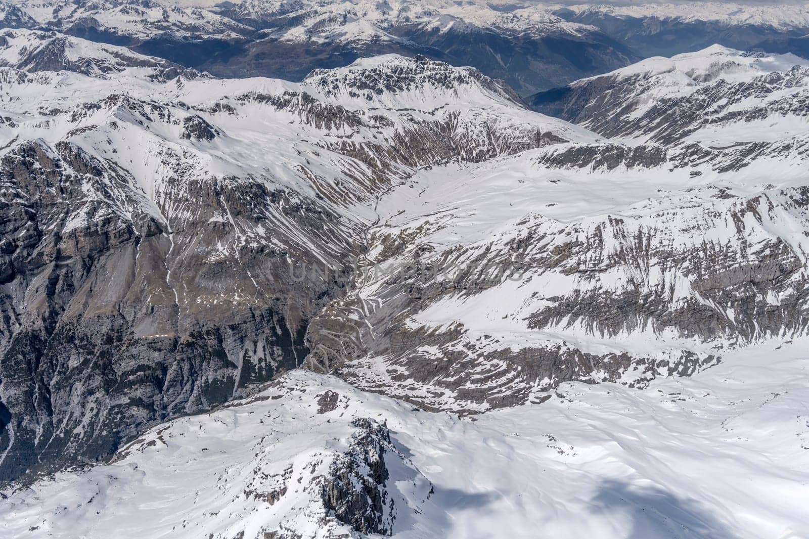 aerial landscape, from a glider plane, of hairpin turns at Stelvio pass road  among rocky snowy slopes, shot from south west in bright late spring light, Sondrio, Italy
