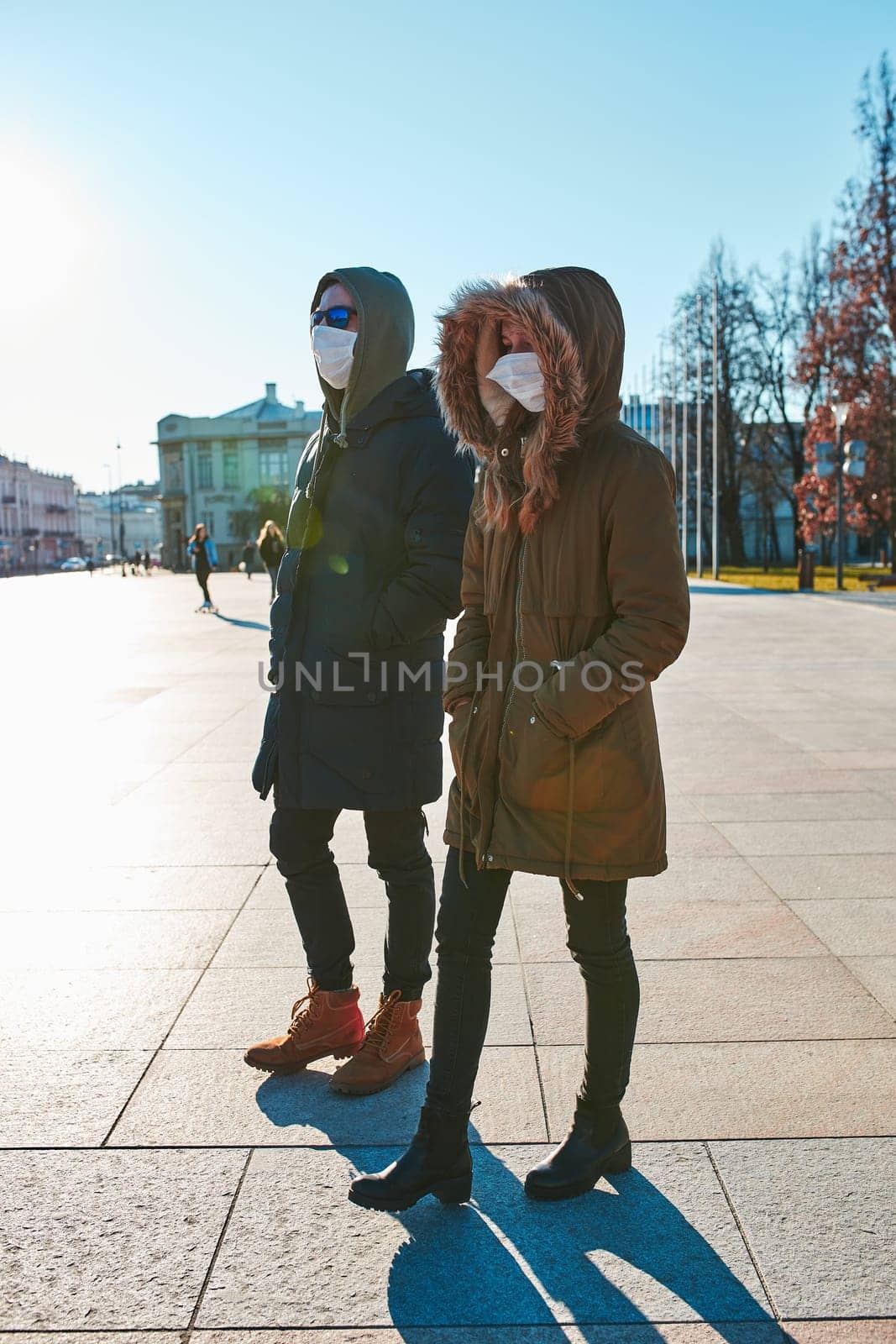 Young woman and man in the hoods wearing the face masks to avoid virus infection and to prevent the spread of disease. People walking in city centre. Virus infection protection. Real people, authentic situations