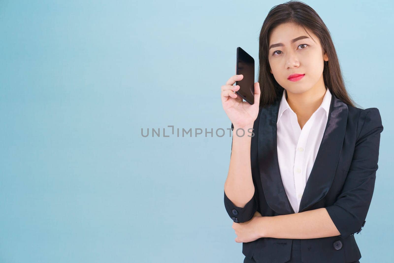 Young women in suit holding her phone standing against blue background