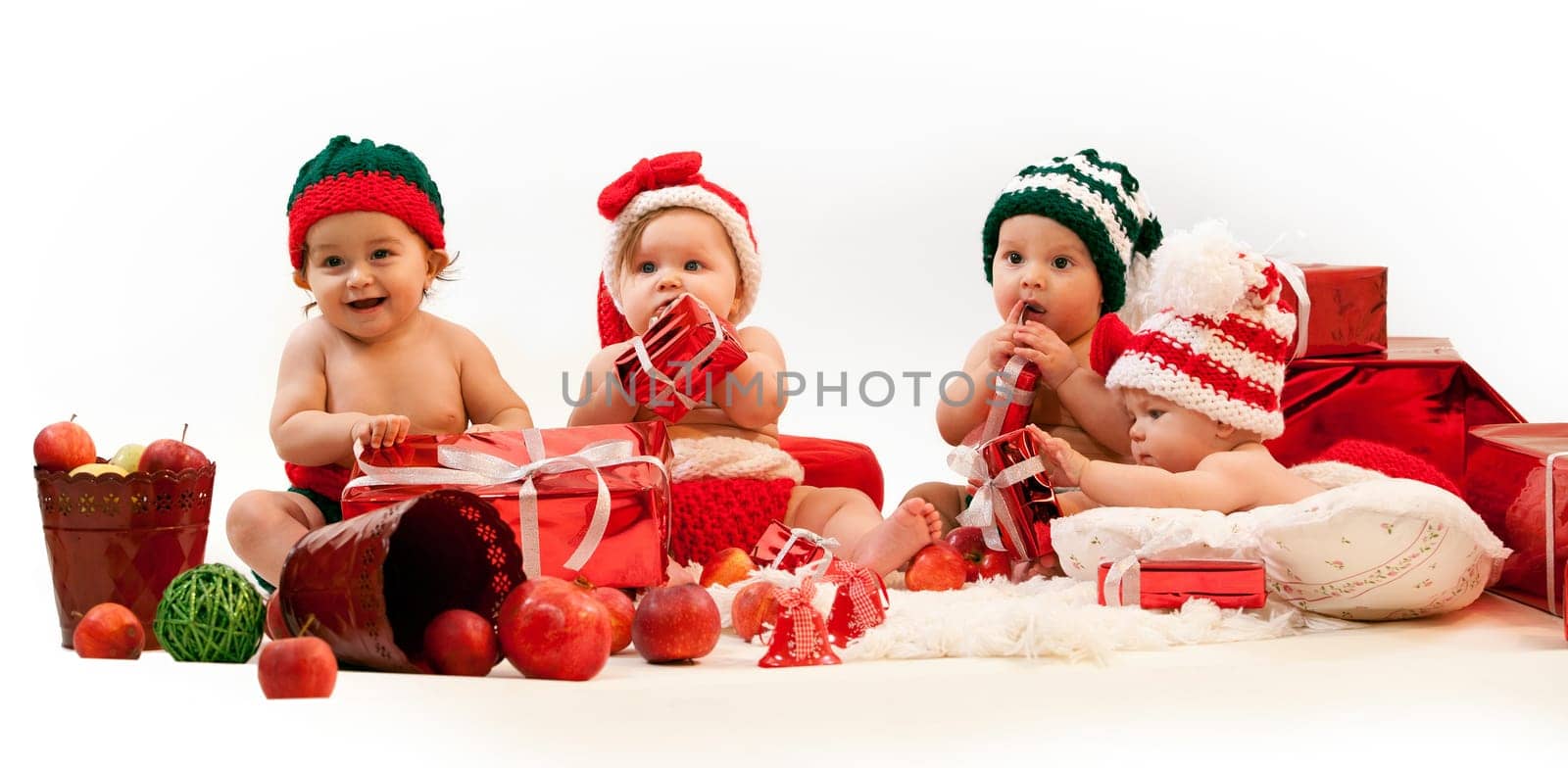 Four cute babies in xmas costumes playing among gifts