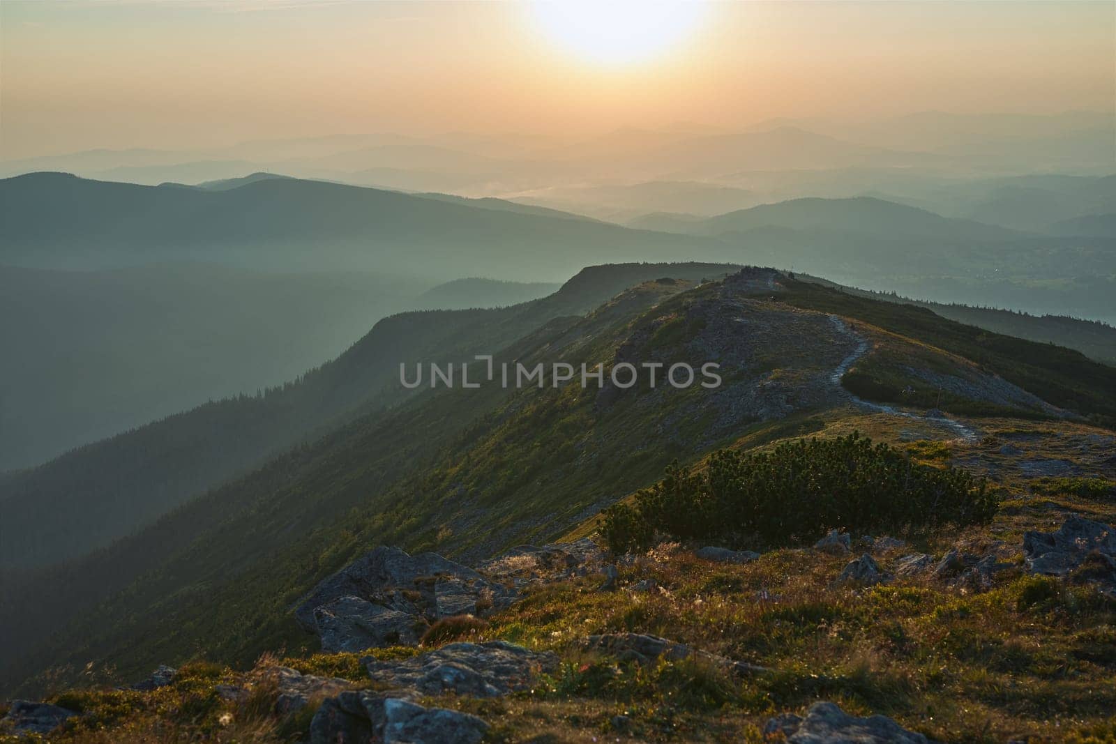Sunrise in mountains. Natural mountain landscape with illuminated misty peaks, foggy slopes and valleys, blue sky with orange yellow sunlight. Amazing scene from Beskid Zywiecki in Poland