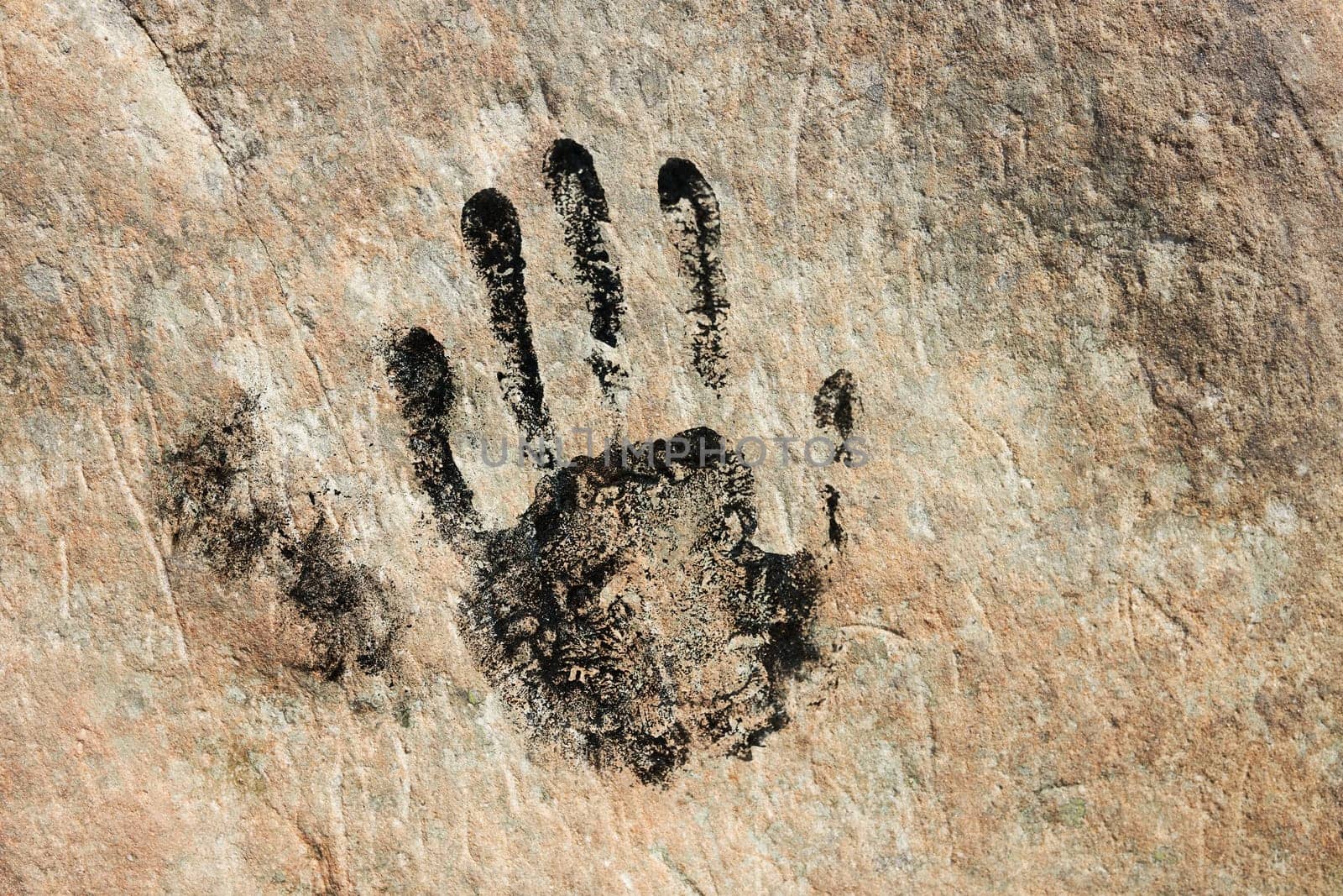 Hand print on sandstone rock. Human imprint on wall. Close up of handmark. Ancient sign. Black print. Identity concept. Tribal art