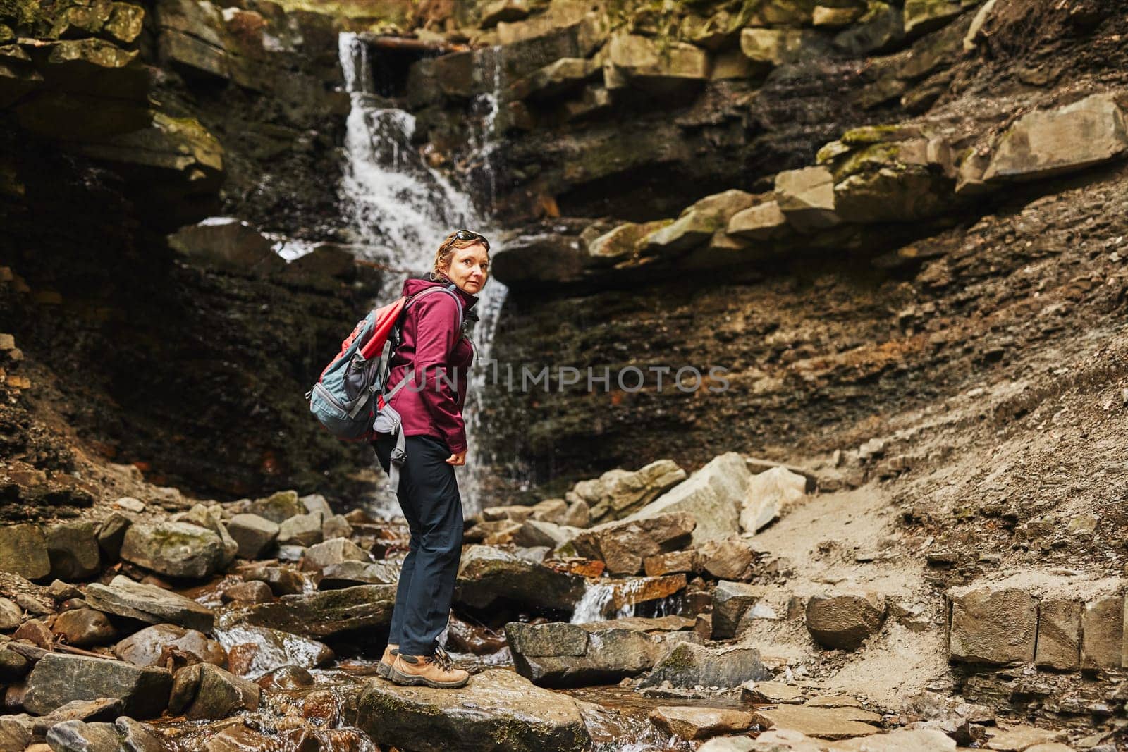 Hiking in mountains. Woman enjoying hike on sunny vacation day. Female with backpack walking close to waterfall. Spending summer vacation close to nature
