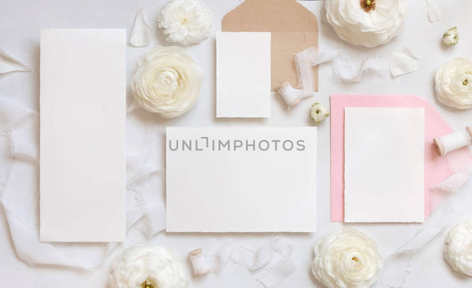 Blank cards and envelopes near cream roses and white silk ribbons top view, mockup. Romantic scene with wedding set and pastel flowers flat lay. Valentines, Spring or Mothers day concept
