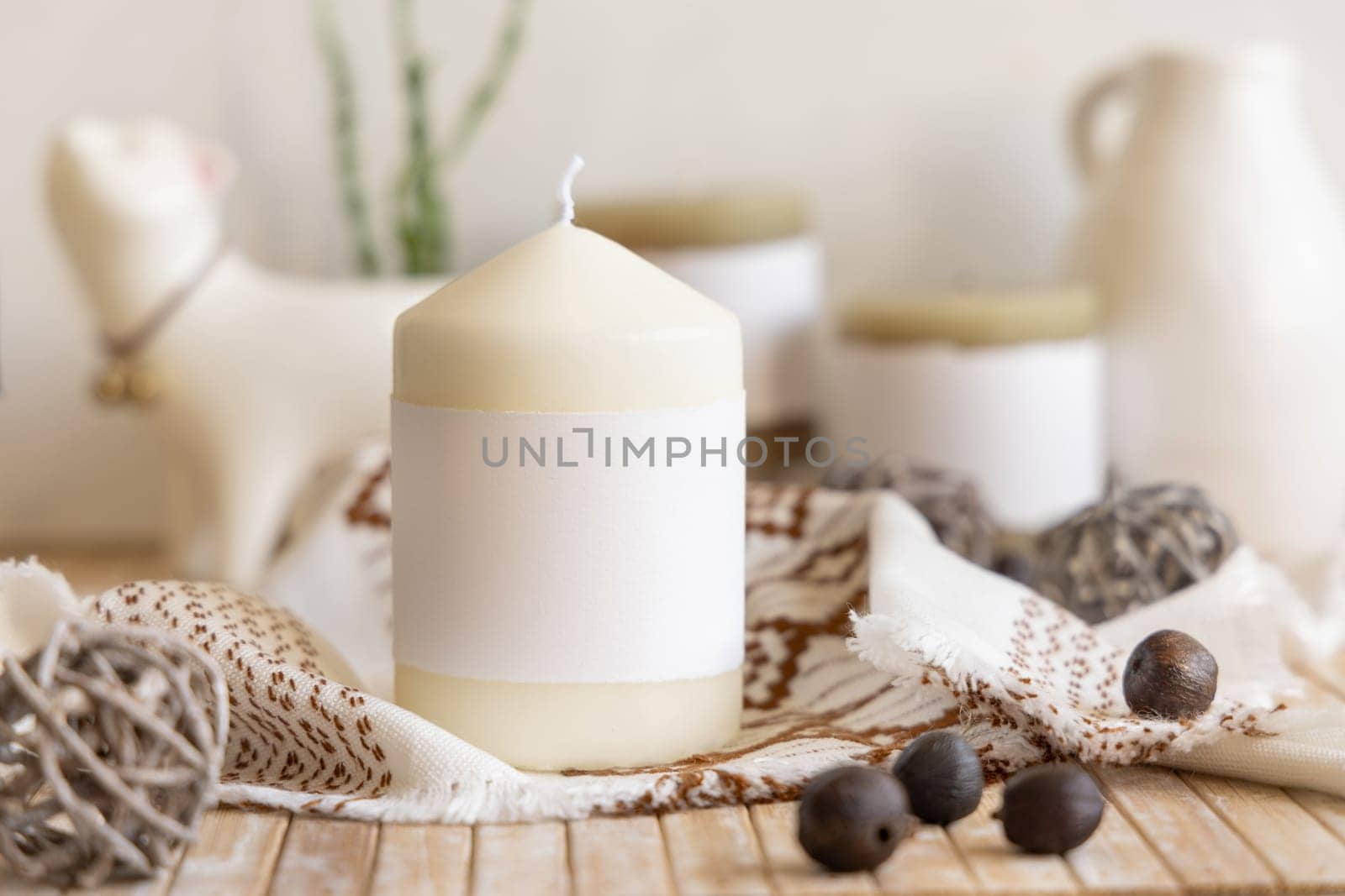 Candle with blank paper label on wooden table near natural decor Close up, copy space. Boho or ethnic packaging mock up. Home decorations in Bohemian or scandinavian style