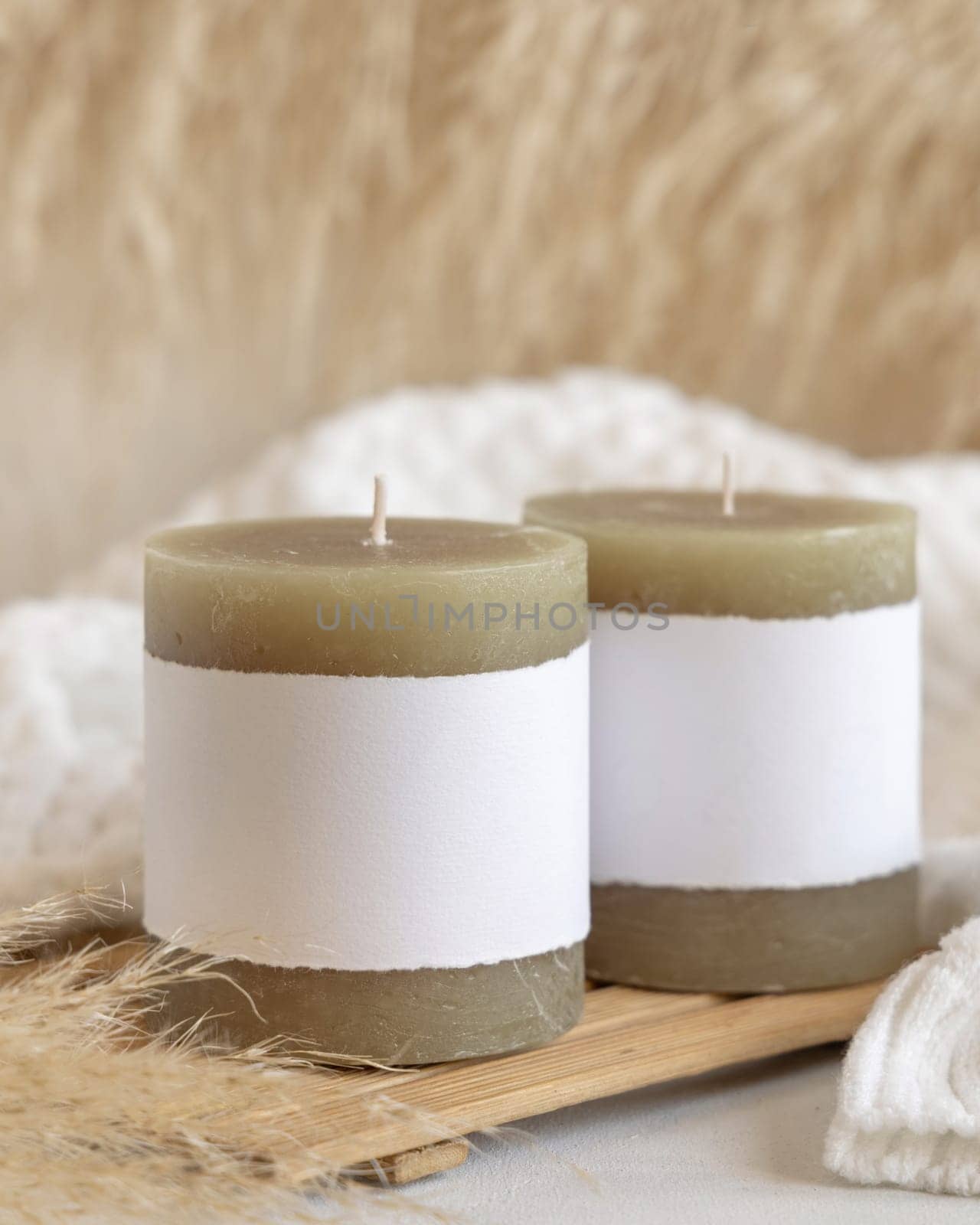 Candles with label on wooden tray near dry pampas grass and cosy white sweater Close up, copy space. Boho packaging mock up. Home decorations, Bohemian, ethnic or scandinavian style
