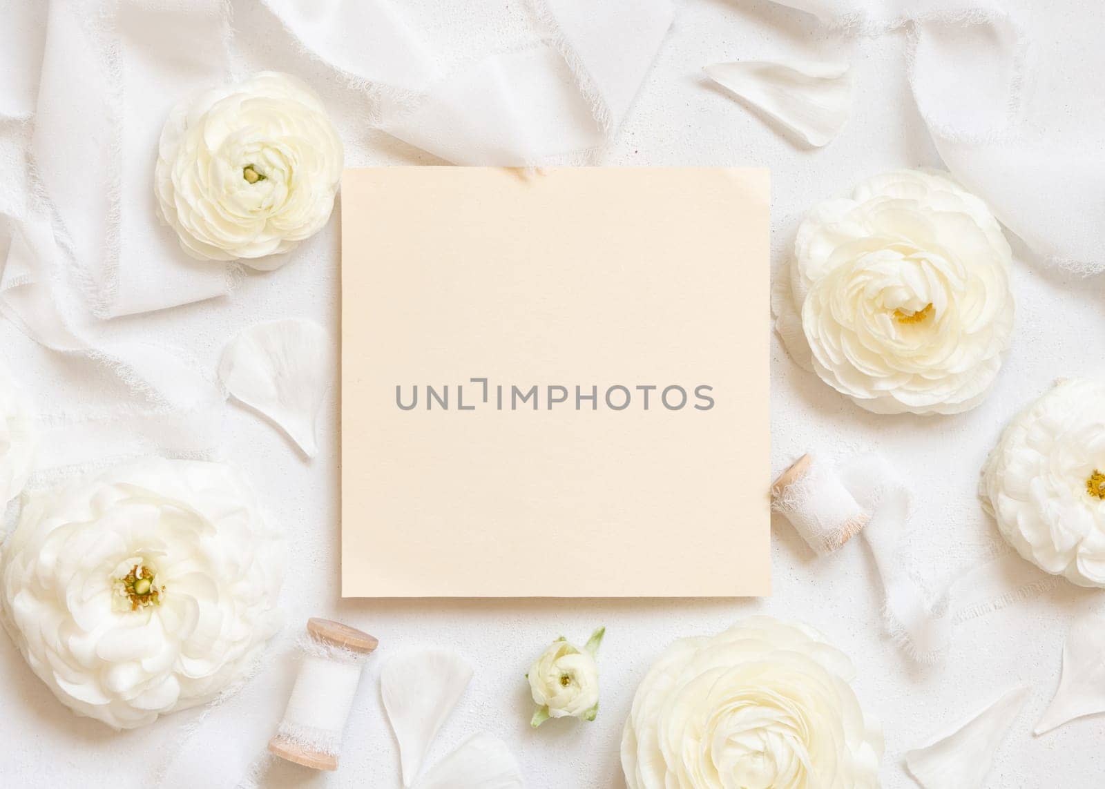 Blank card near cream roses and white silk ribbons top view, wedding mockup. Romantic scene with square card and pastel flowers flat lay. Valentines, Spring or Mothers day concept