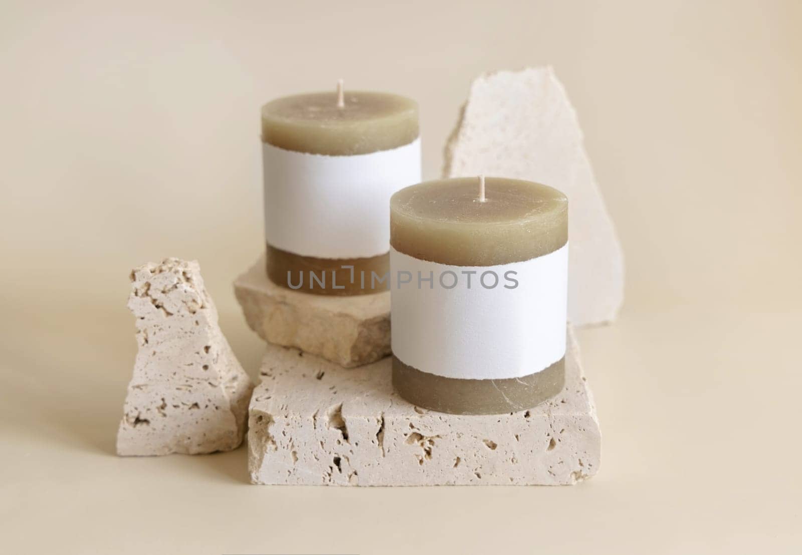 Candles with label on beige near cream travertine stones, Close up, copy space. Brand packaging mock up. Home decoration, minimal interior, Bohemian or scandinavian style