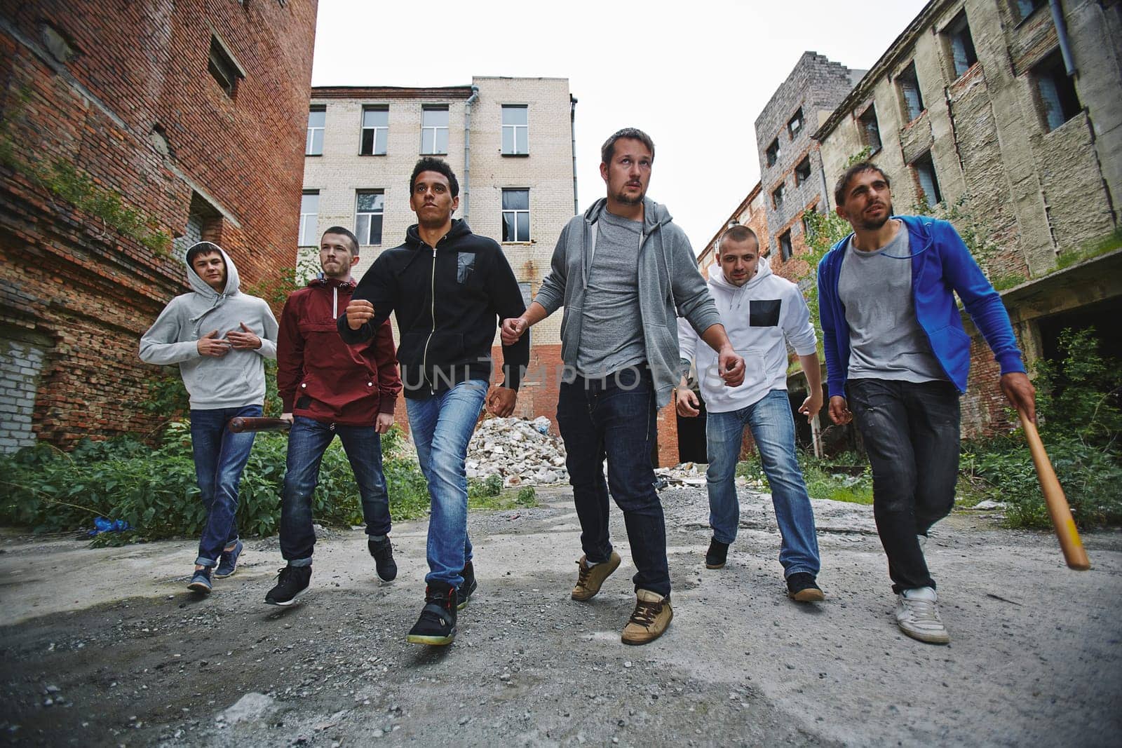 Group of spiteful hooligans walking along grunge brick houses