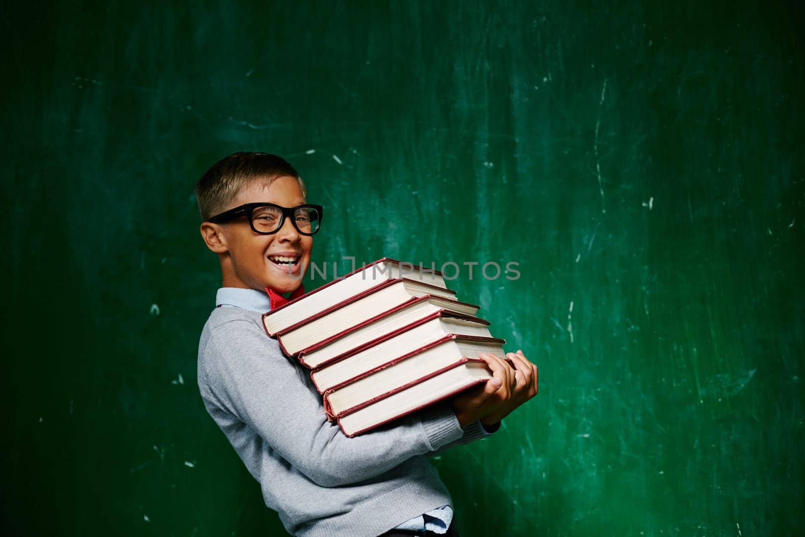 Cheerful schoolkid with stack of books looking at camera