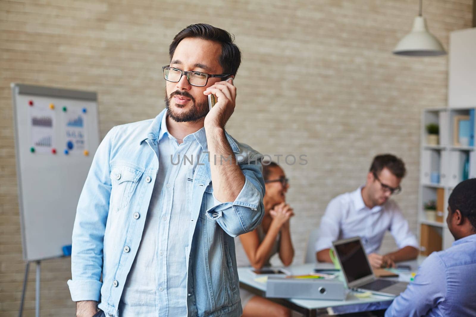 Asian businessman in eyeglasses speaking on cellphone in working environment