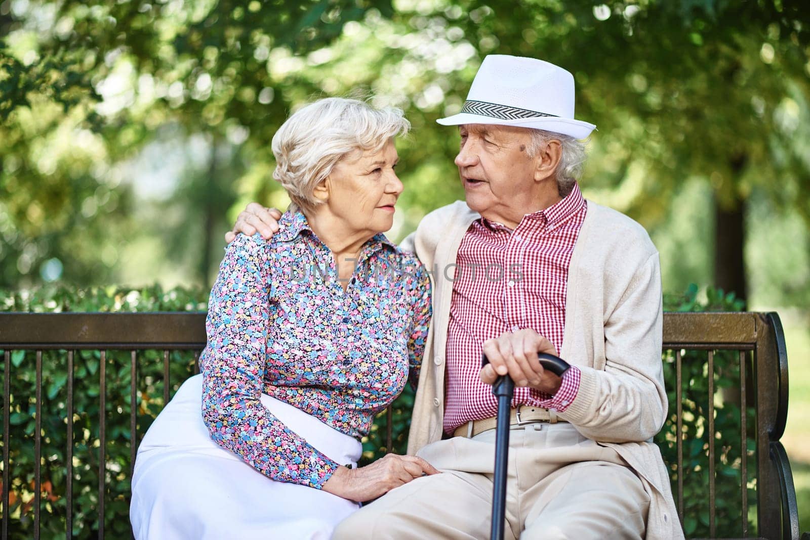Restful seniors in smart casual sitting on bench in park and talking