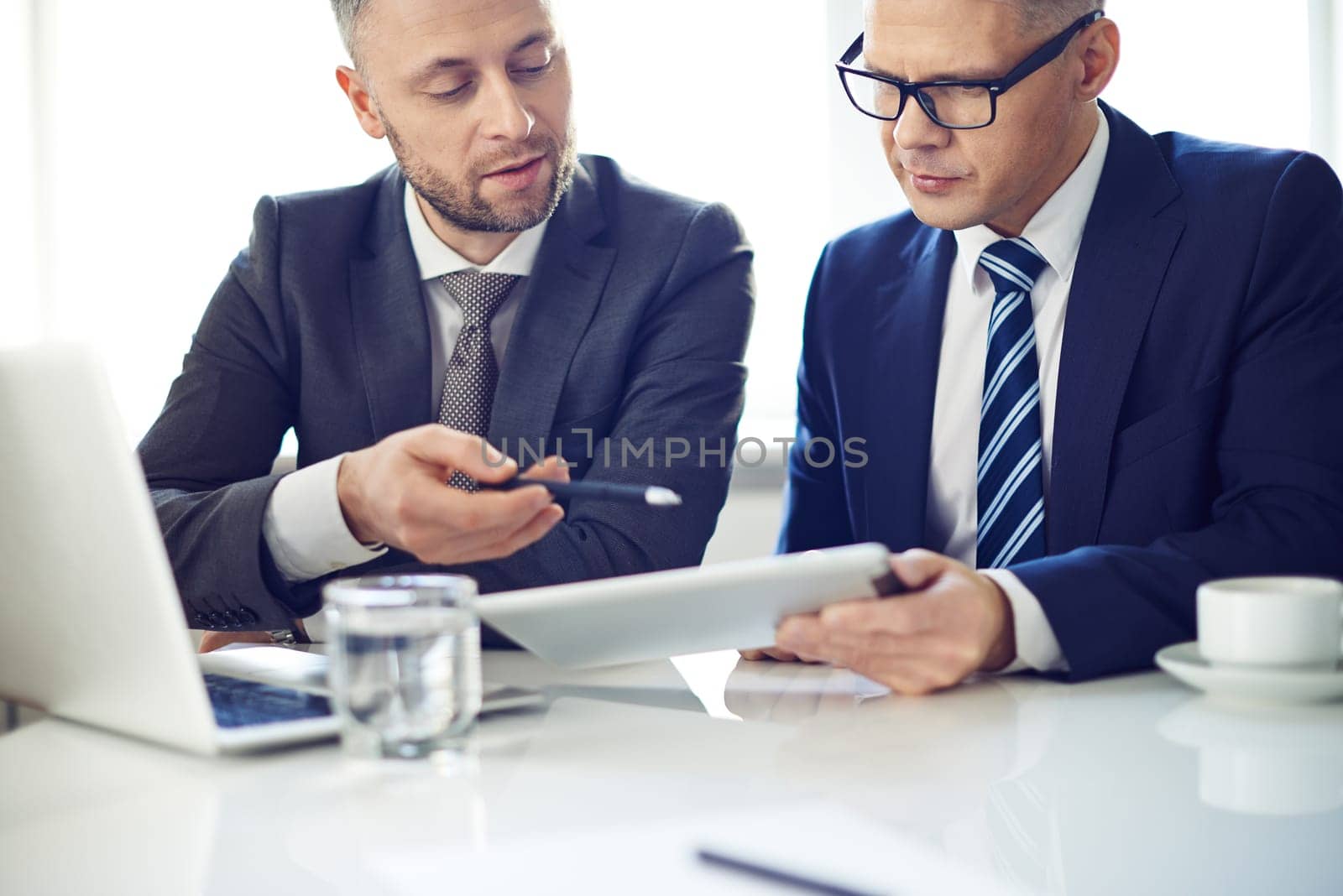 Two elegant men using digital tablet at meeting