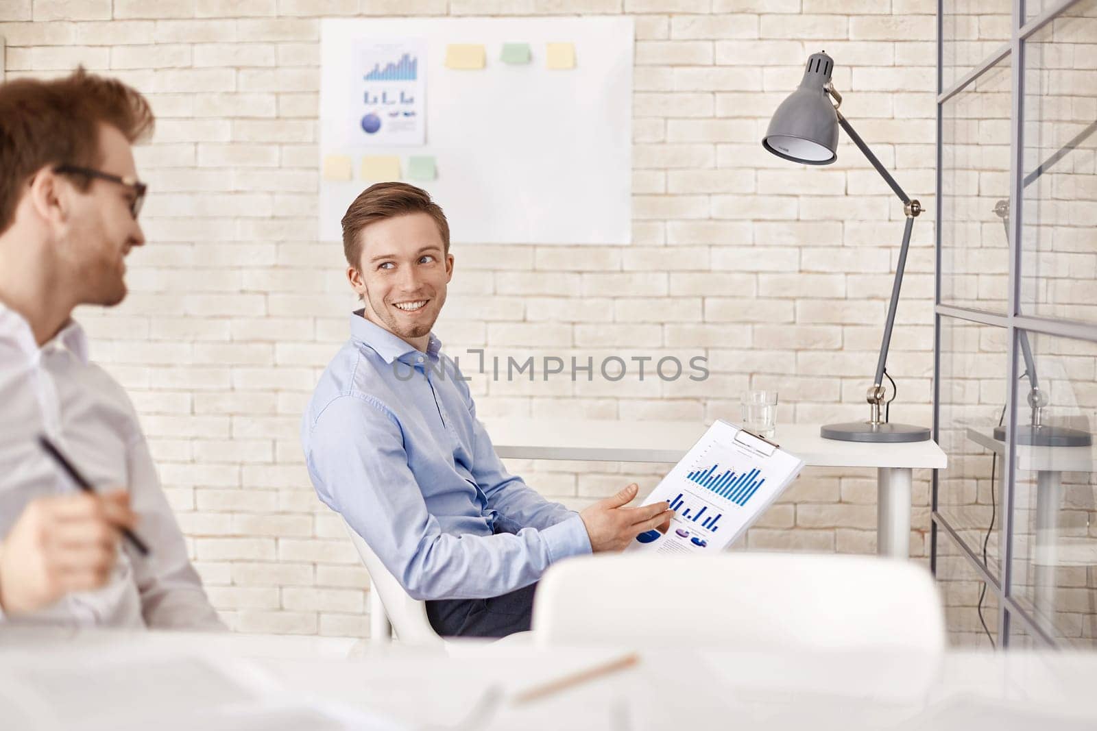 Happy businessman with financial document pointing at it while looking at his co-worker