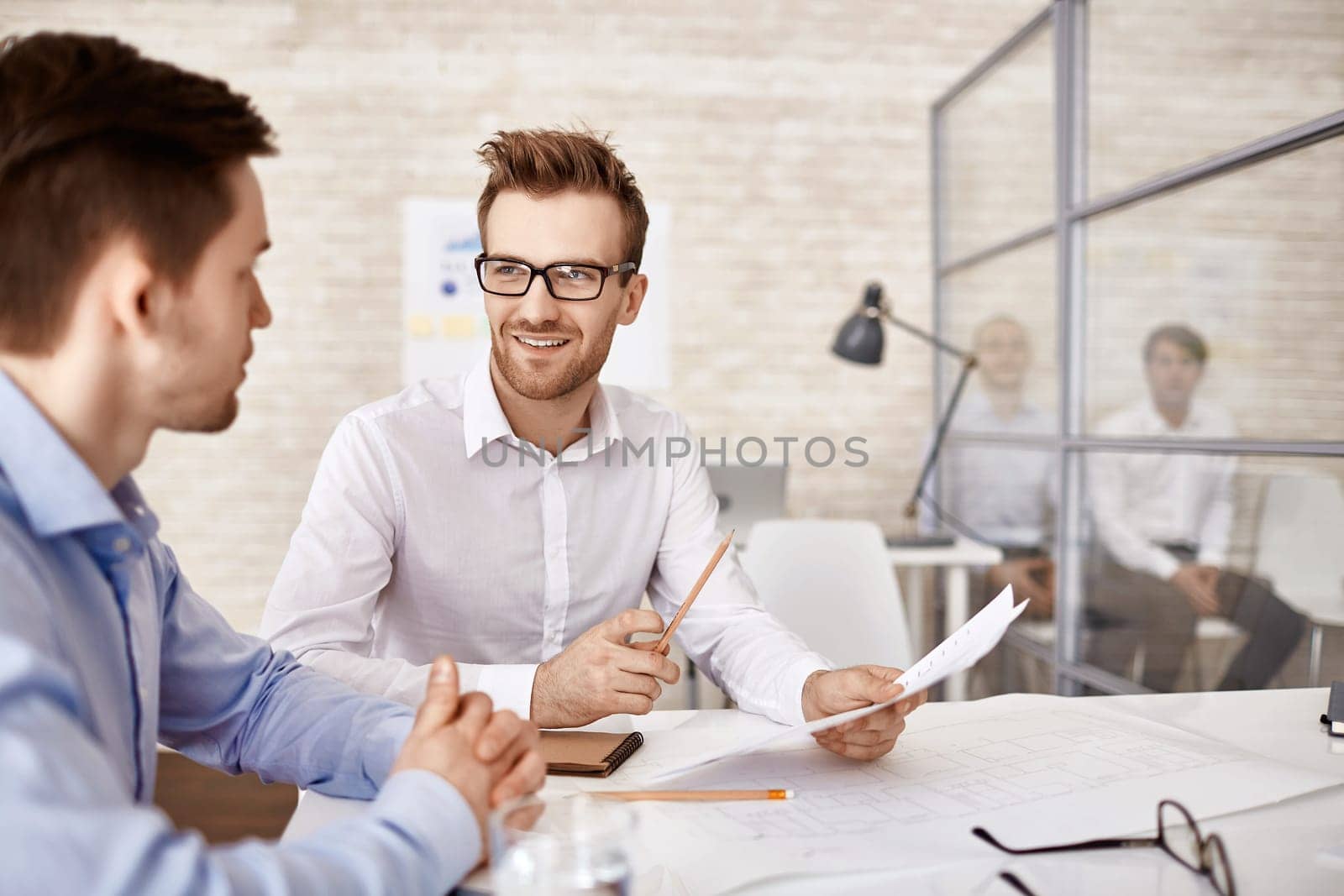 Young businessman in eyeglasses talking to his co-worker at meeting