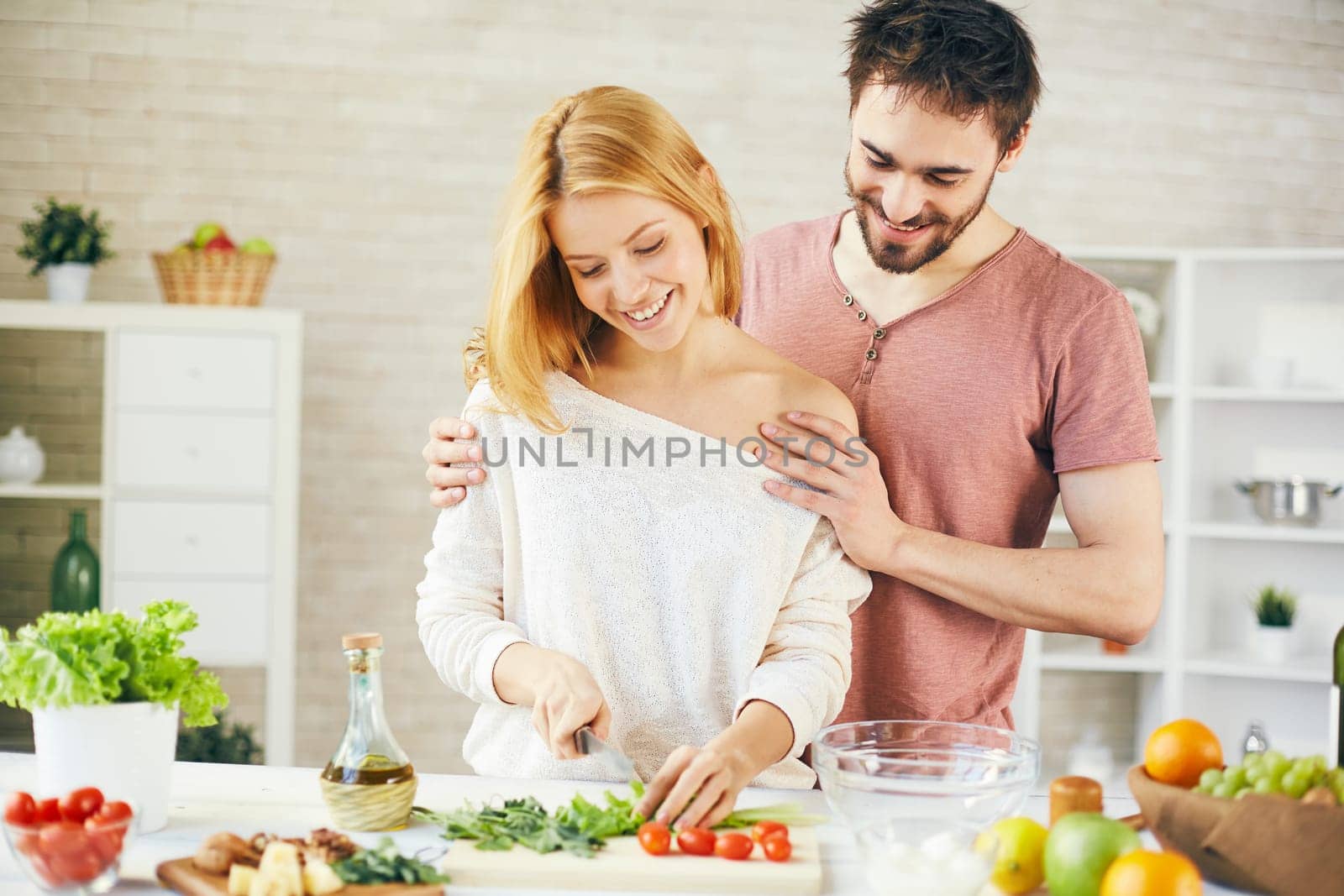 Pretty woman cutting lettuce for vegetable salad with her husband near by