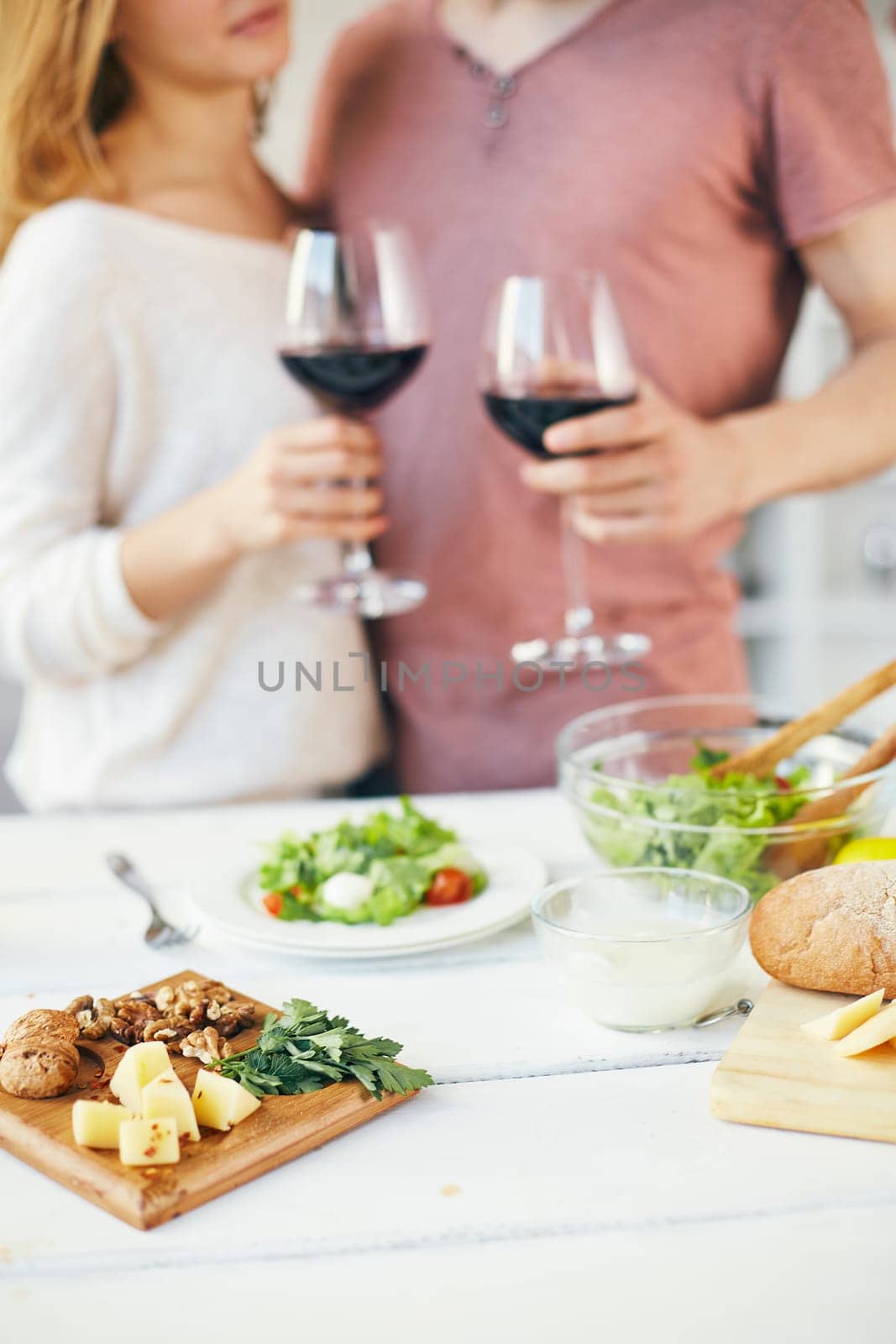 Walnuts, cheese and green parsley on the table and toasting couple on background