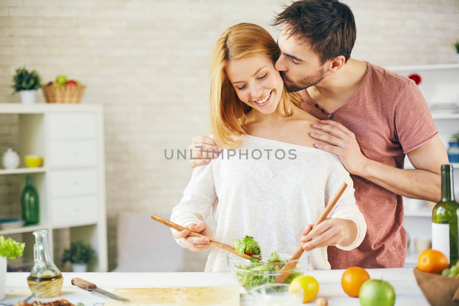 Affectionate young man kissing his wife while she cooking salad