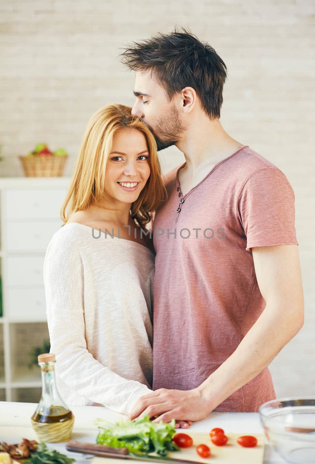 Happy young woman looking at camera while her sweetheart kissing her hair