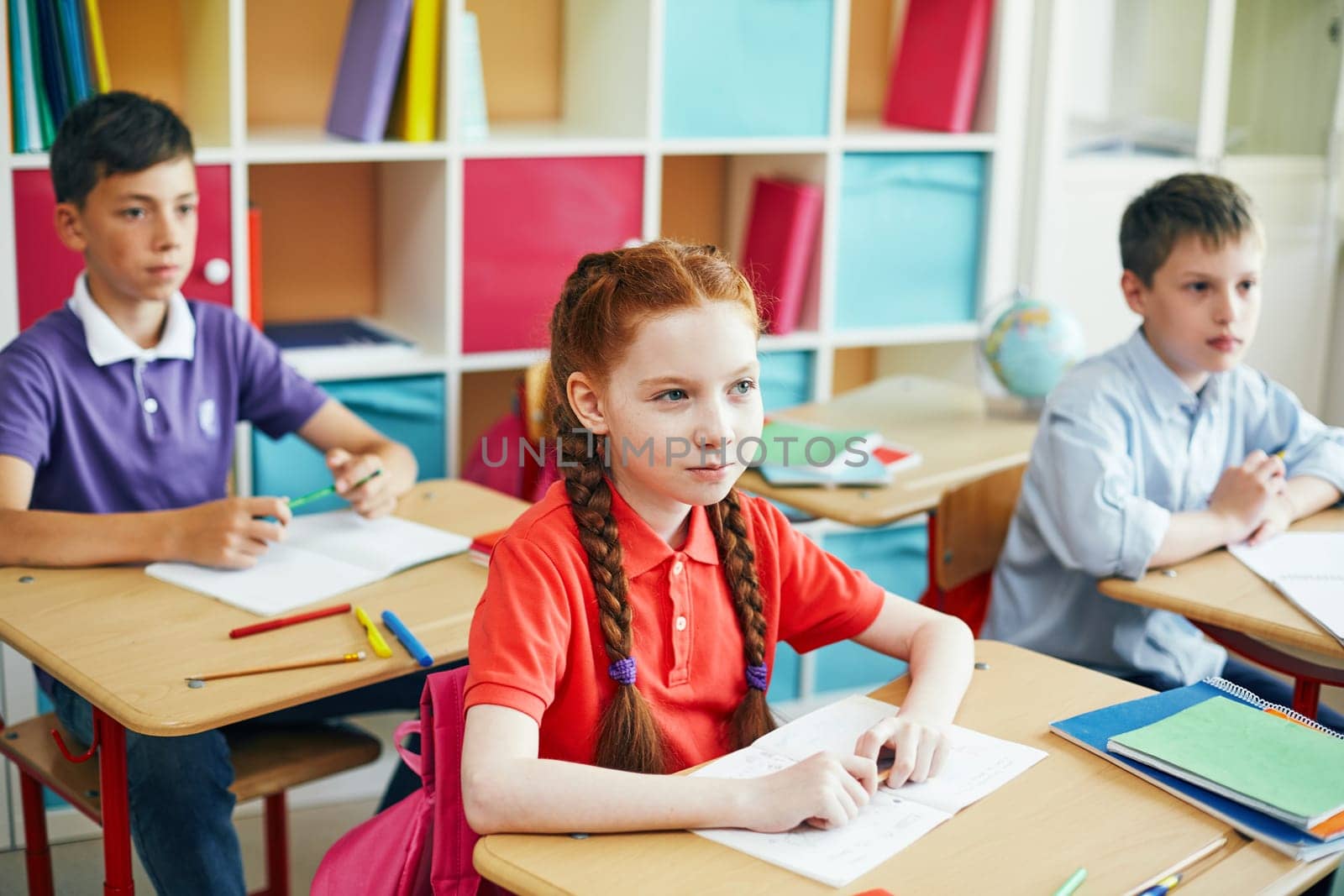 Serious schoolgirl and her classmates listening to their teacher at lesson