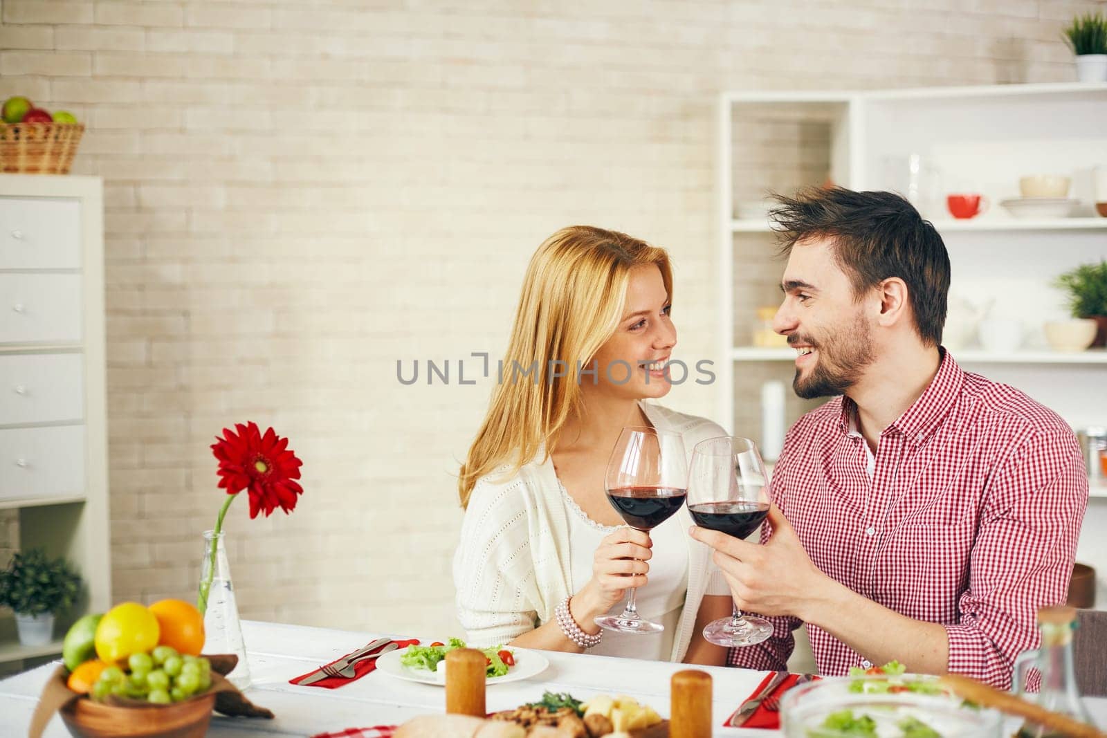 Happy young couple toasting with red wine by breakfast