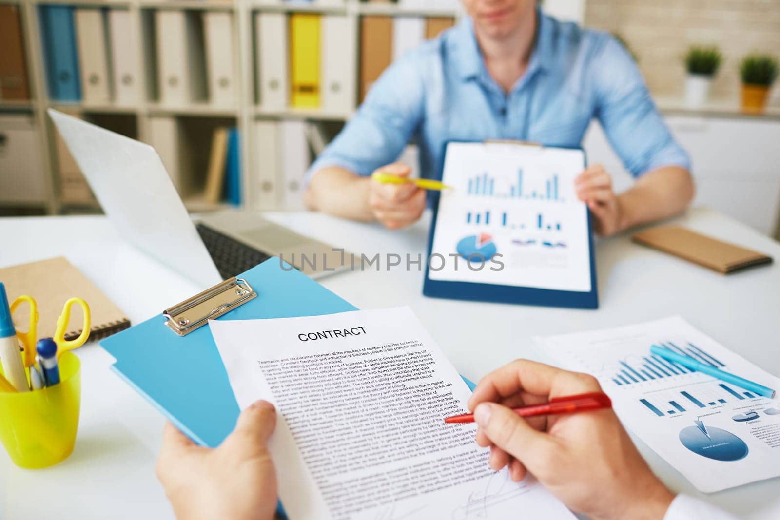 Businessman signing agreement on background of his colleague pointing at document