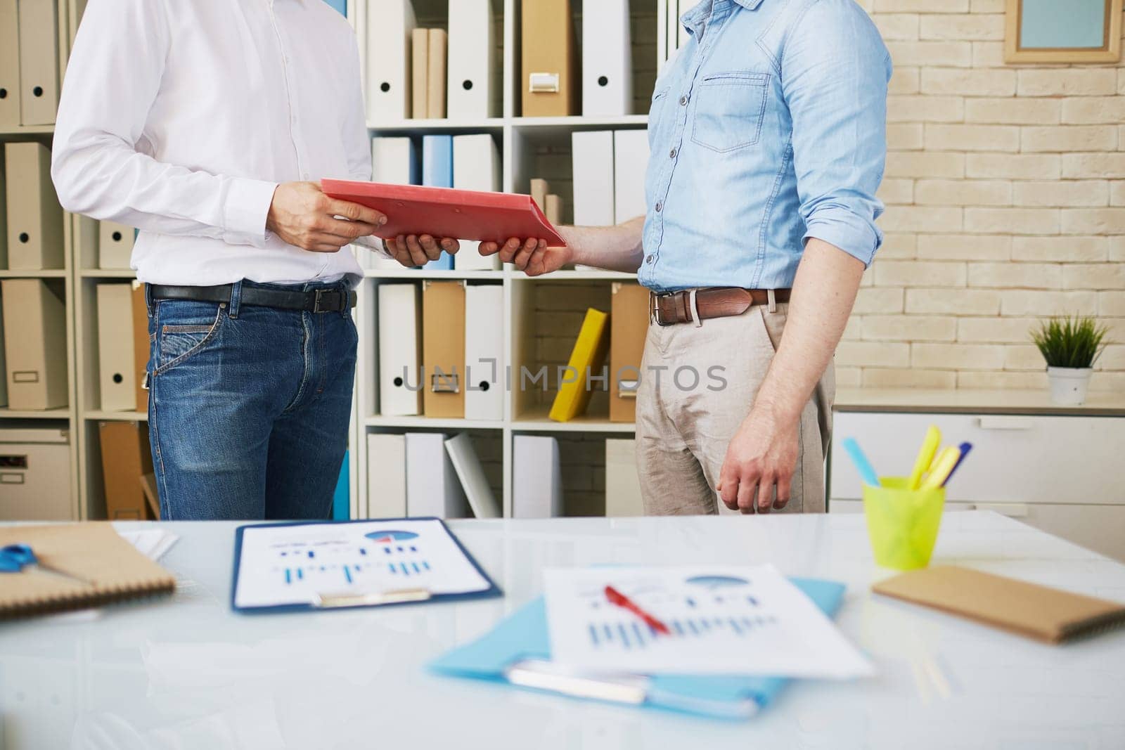 Male employee giving clipboard with papers to his colleague in office