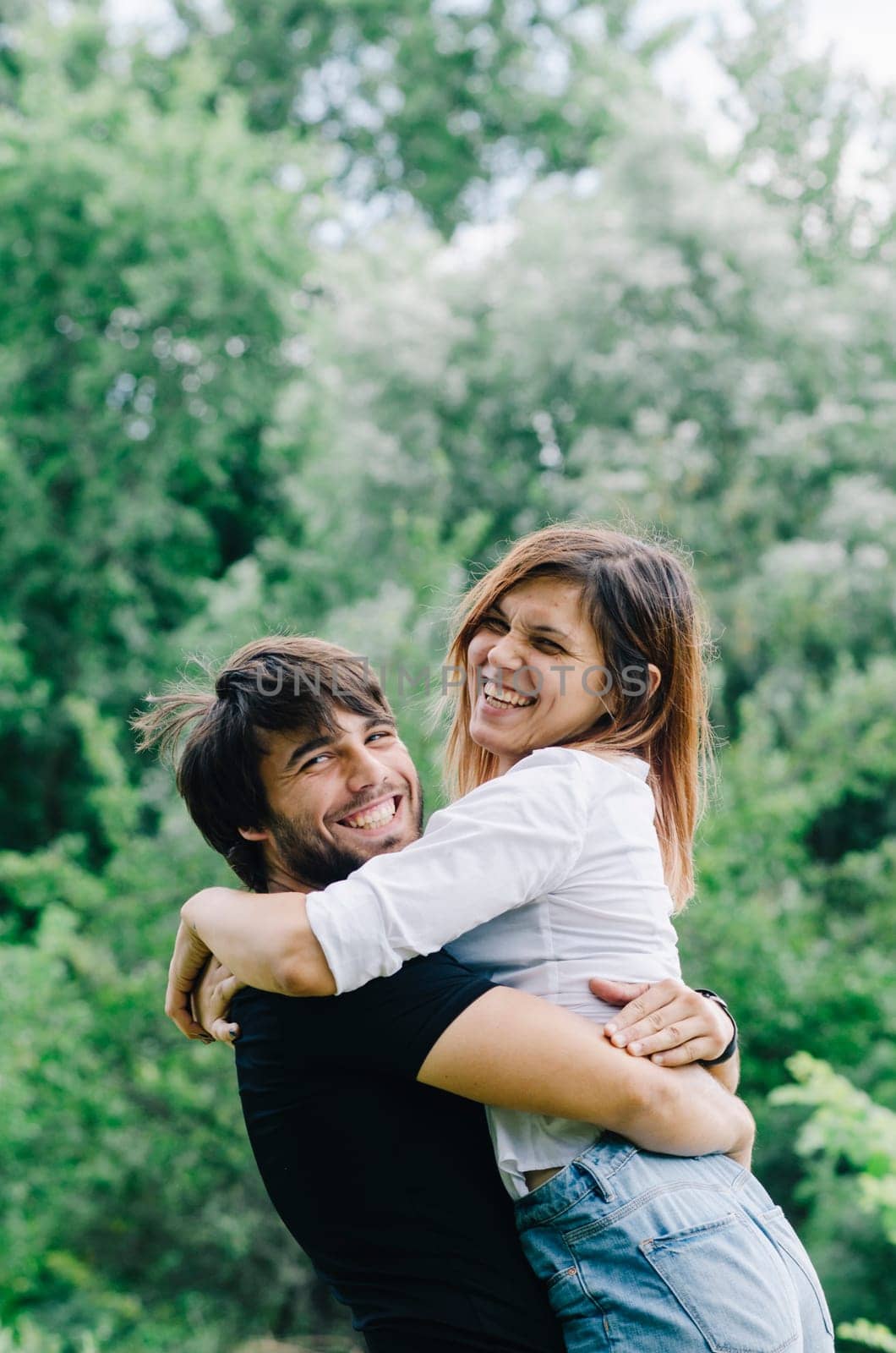 Happy couple kissing and hugging in nature. Young man and woman in loving relationship having fun in park. Boyfriend and girlfriend show emotions and caring.