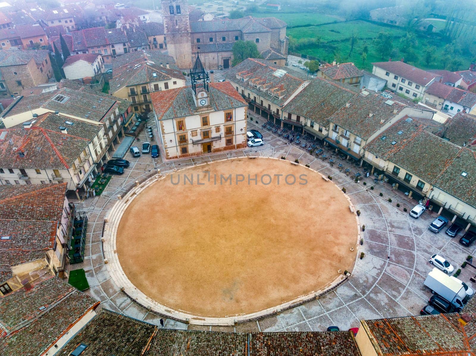 City Hall In Town Square Of Riaza Cradle Of The Red Villages In addition Of Beautiful Medieval Town In Segovia,  with a church in the background on a day with thick fog and mystical atmosphere. Spain