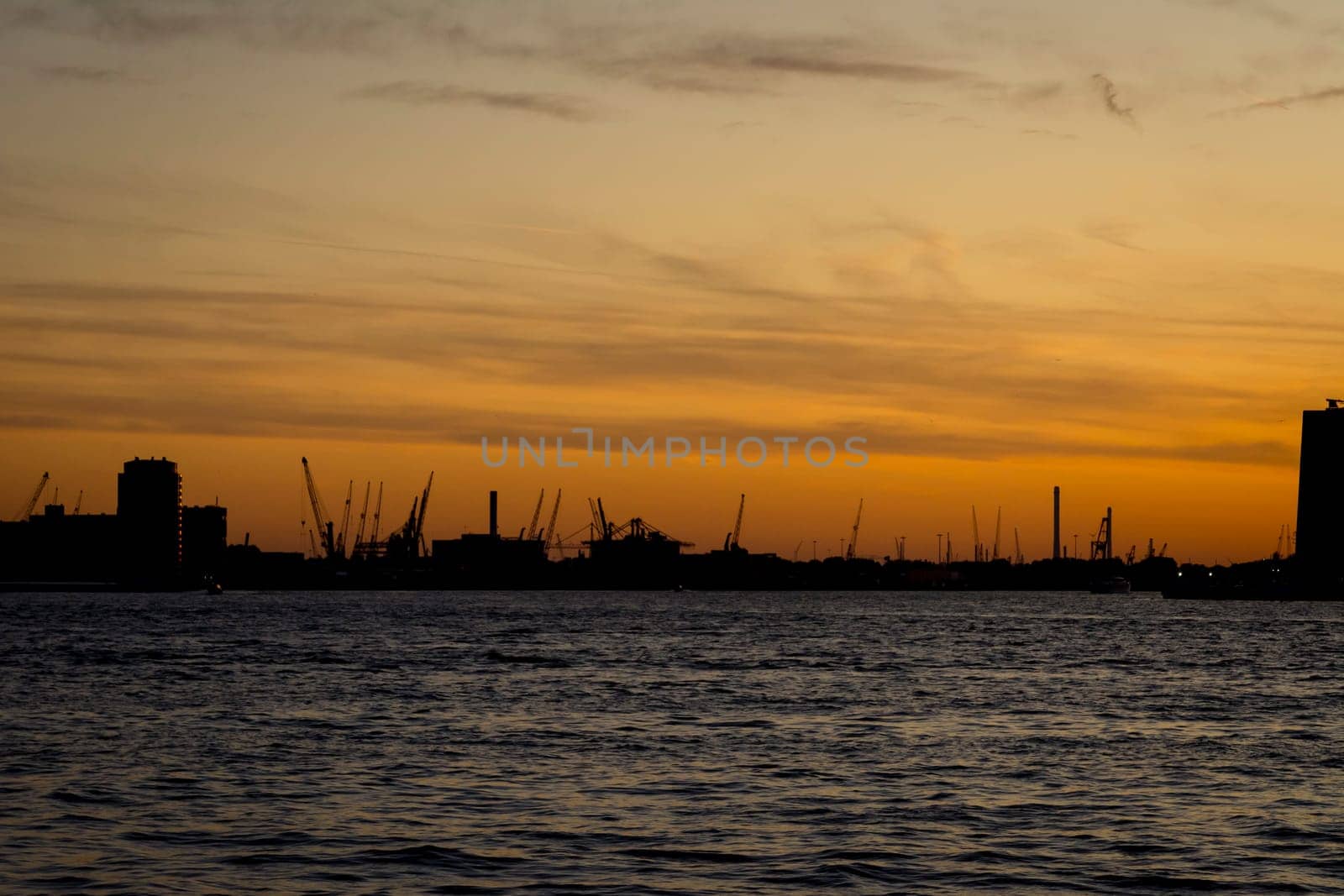 Silhouette of Rotterdam port in the Netherlands during an orange sunset.